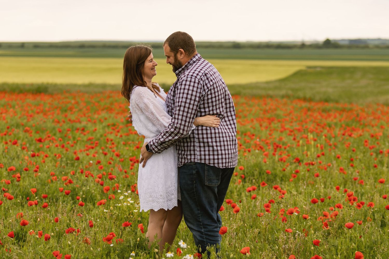 Romantic couple standing face to face in a lush red poppy flower field outdoors.