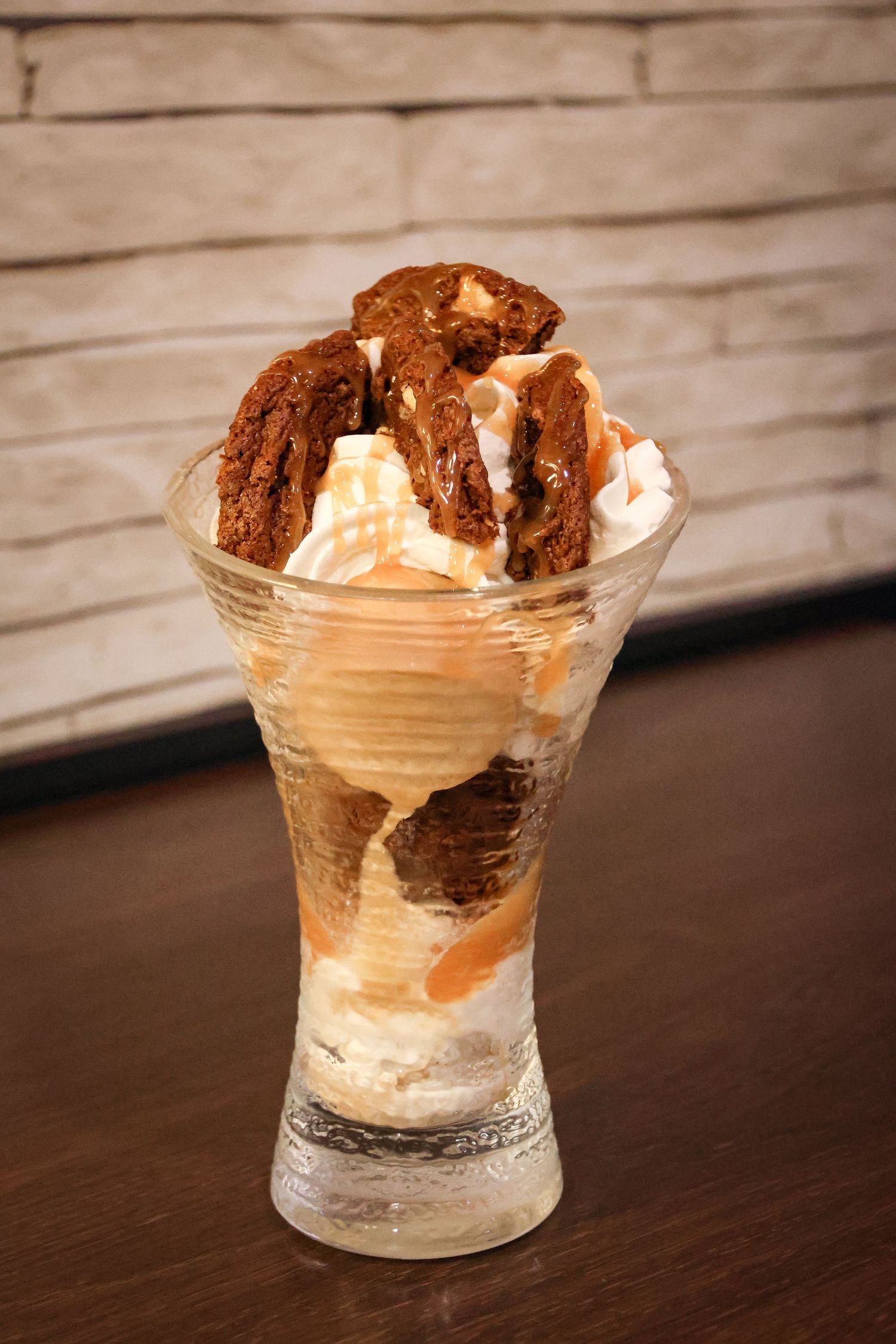 A glass sundae with vanilla and chocolate ice cream scoops, caramel sauce, whipped cream, and chocolate cookies on top.