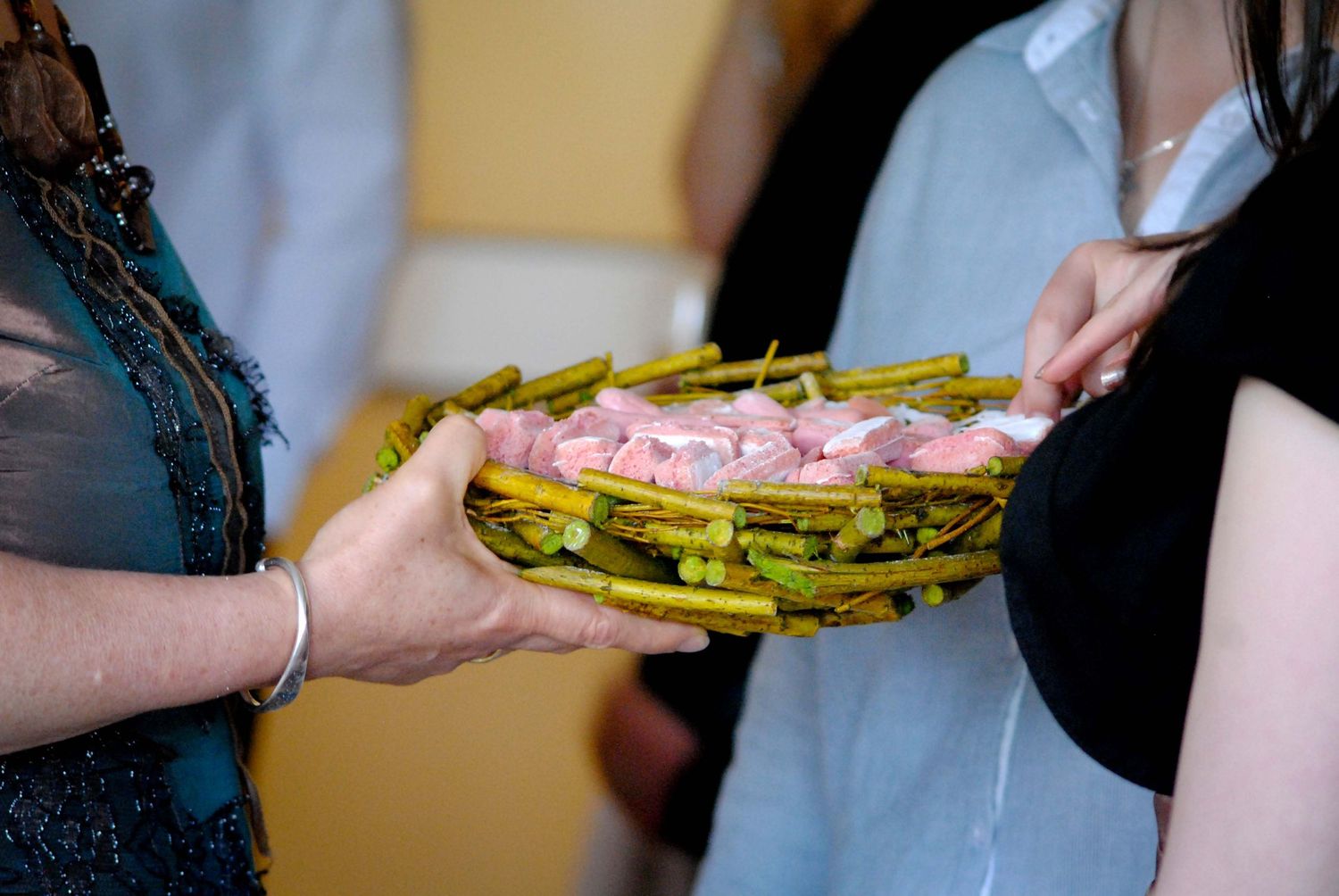 Hands holding a woven basket tray with pink appetizers and green asparagus spears at a catered event.