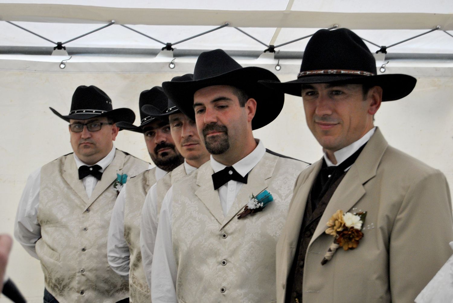 Four groomsmen in matching cream vests and black cowboy hats stand together at a western-themed wedding ceremony.