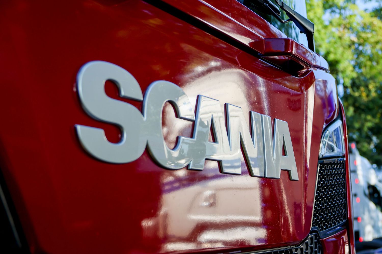 Close-up of chrome SCANIA lettering badge on a glossy red truck cab in sunlight.