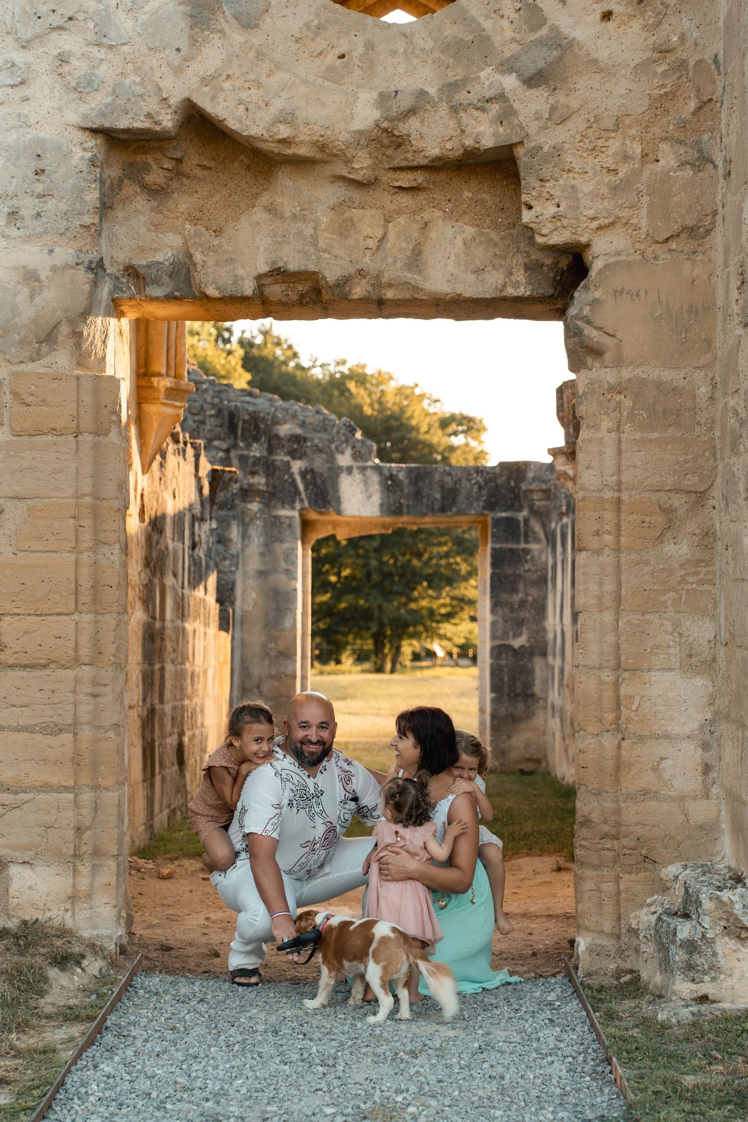 A loving family with two children and a dog poses inside an ancient stone archway at sunset.