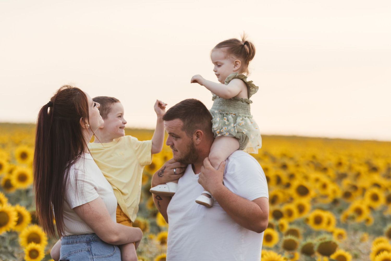 Happy family with two toddlers enjoying a sunny sunflower field at sunset.