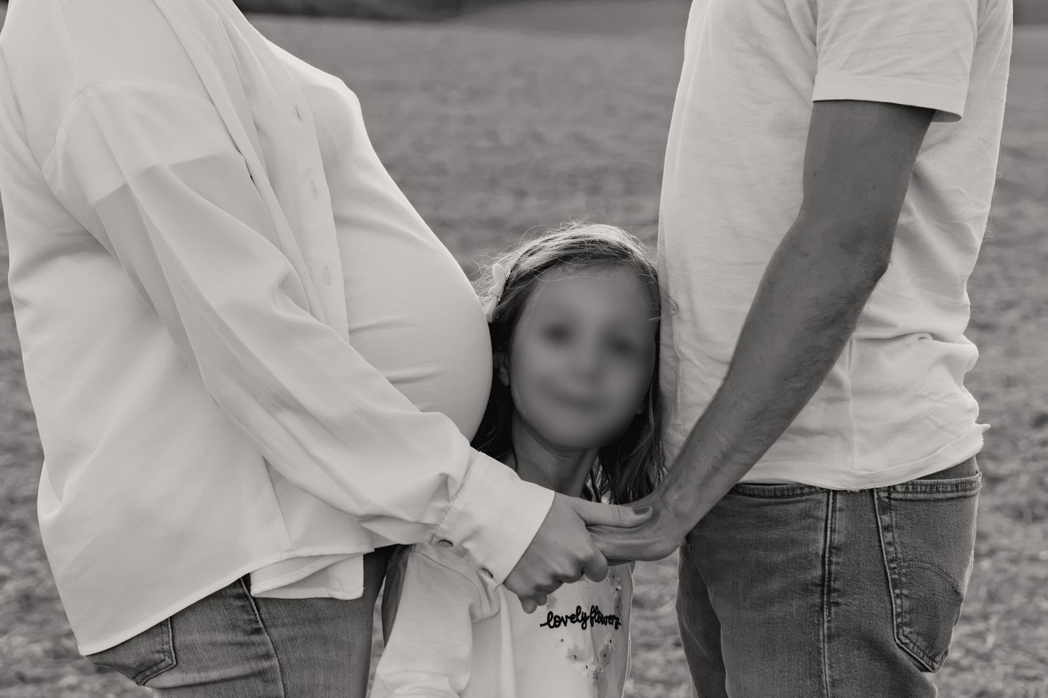 Black and white family maternity photo with parents holding hands with young child outdoors.