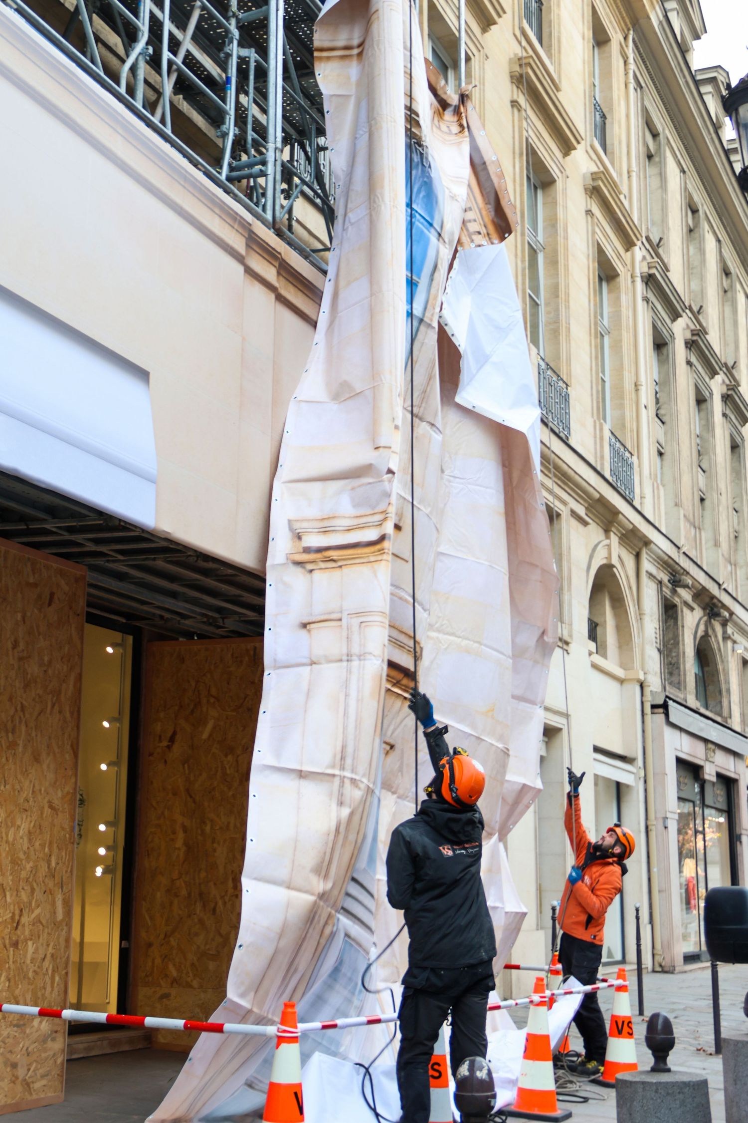 Workers in orange safety gear removing large decorative facade panels from a Parisian building street renovation.