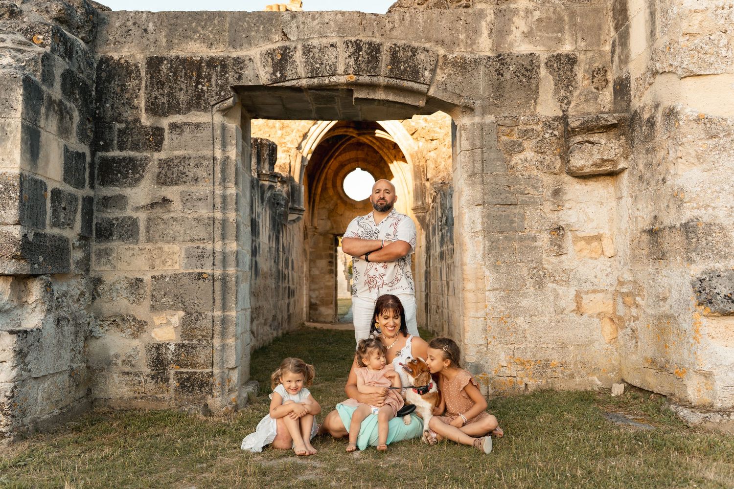 Family of five with young children gathered around a mother and baby in scenic historic stone ruins.