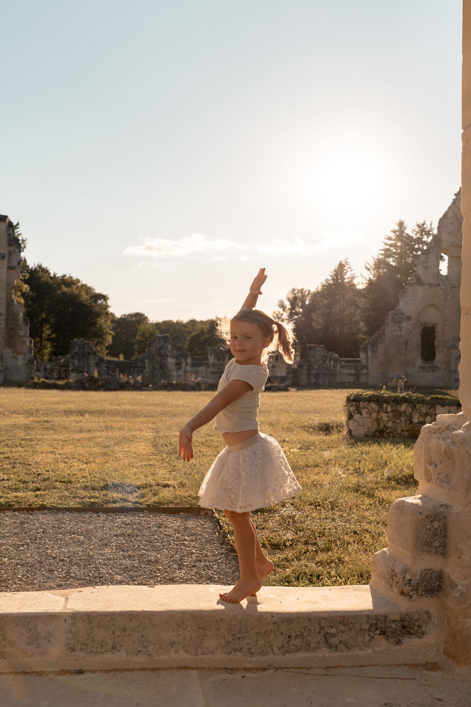 A joyful barefoot girl in a tutu skirt poses gracefully at sunset among historic stone ruins.