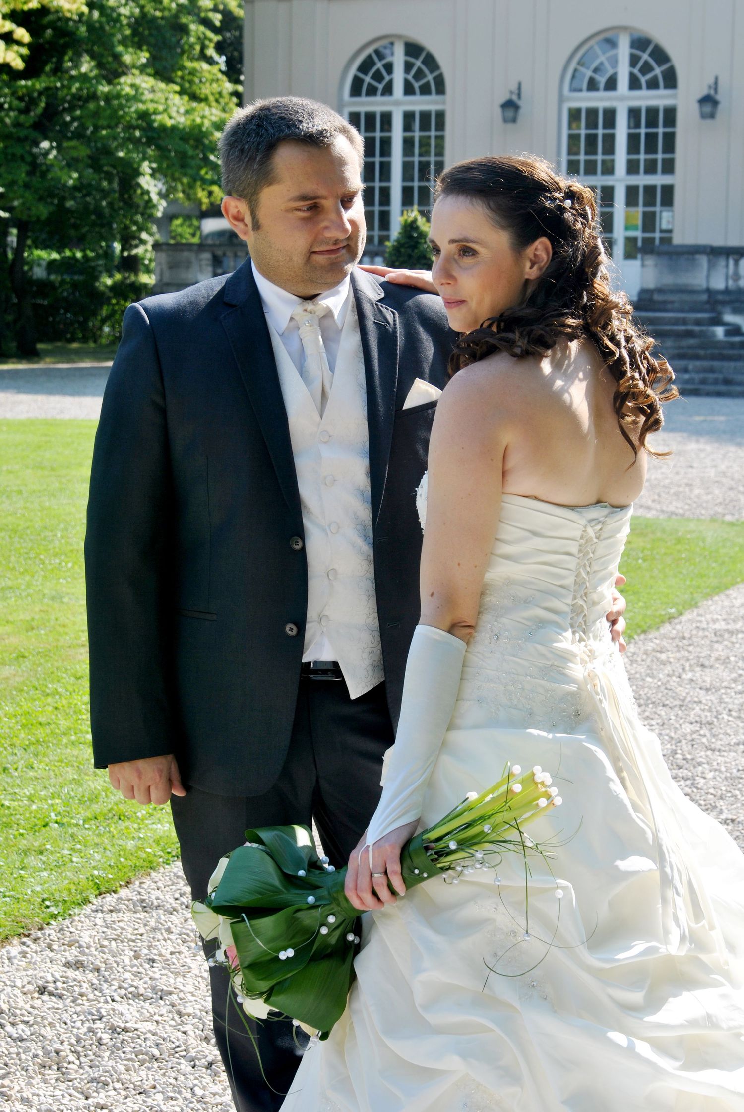 Bride and groom exchange glances outdoors near a historic building.
