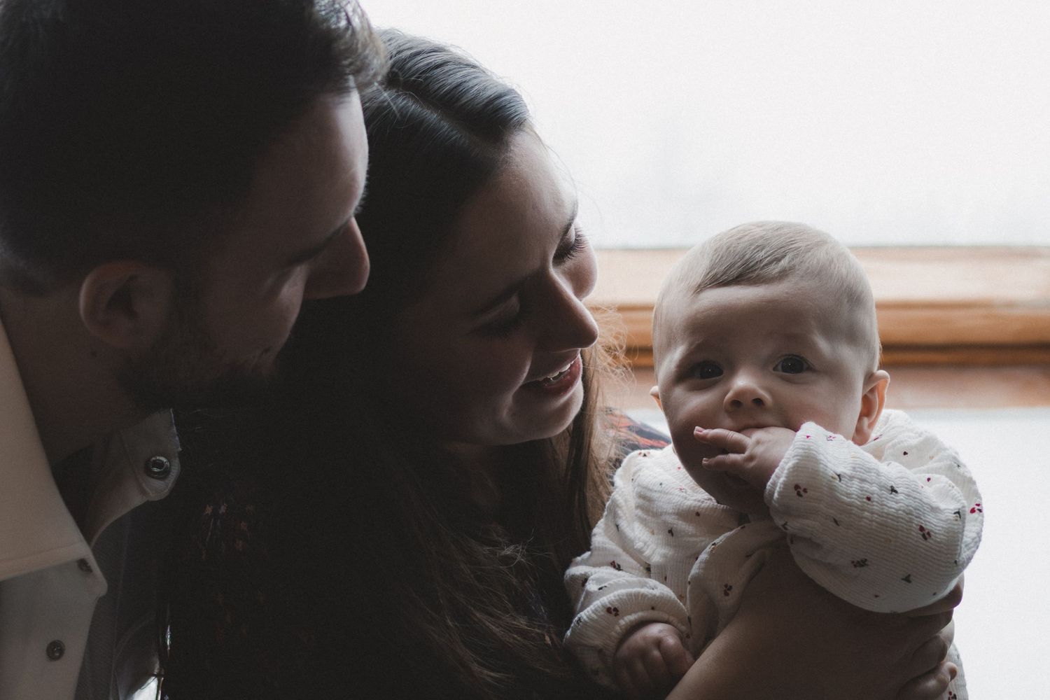 Happy young parents smiling at their adorable baby, sharing a tender family moment together indoors.