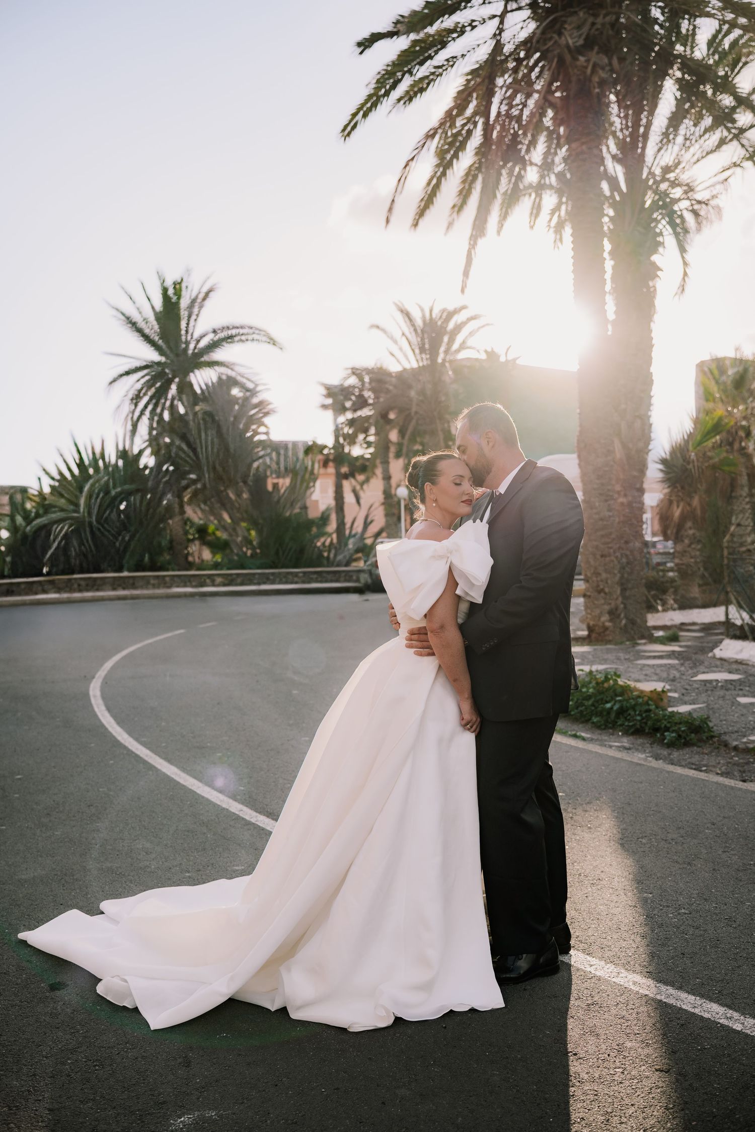 A romantic sunset wedding photo series shows a couple embracing on a palm-lined road.