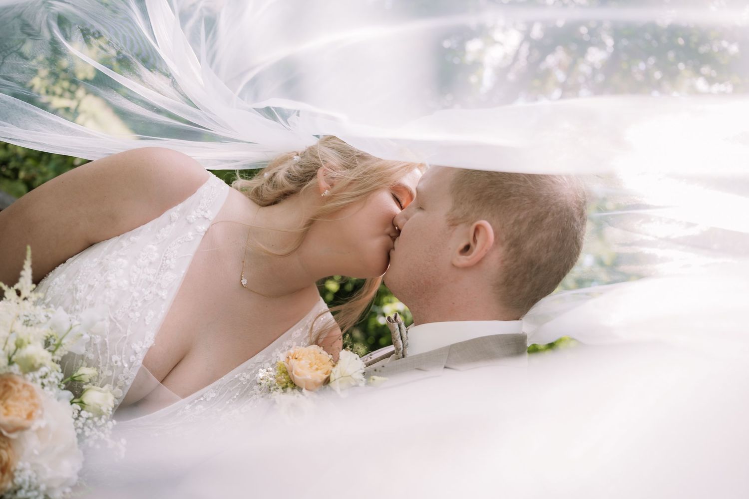 Hochzeitsfotograf Heilbronn,StuttgartBride and groom sharing a romantic kiss under a flowing white veil, surrounded by soft floral bouquets.