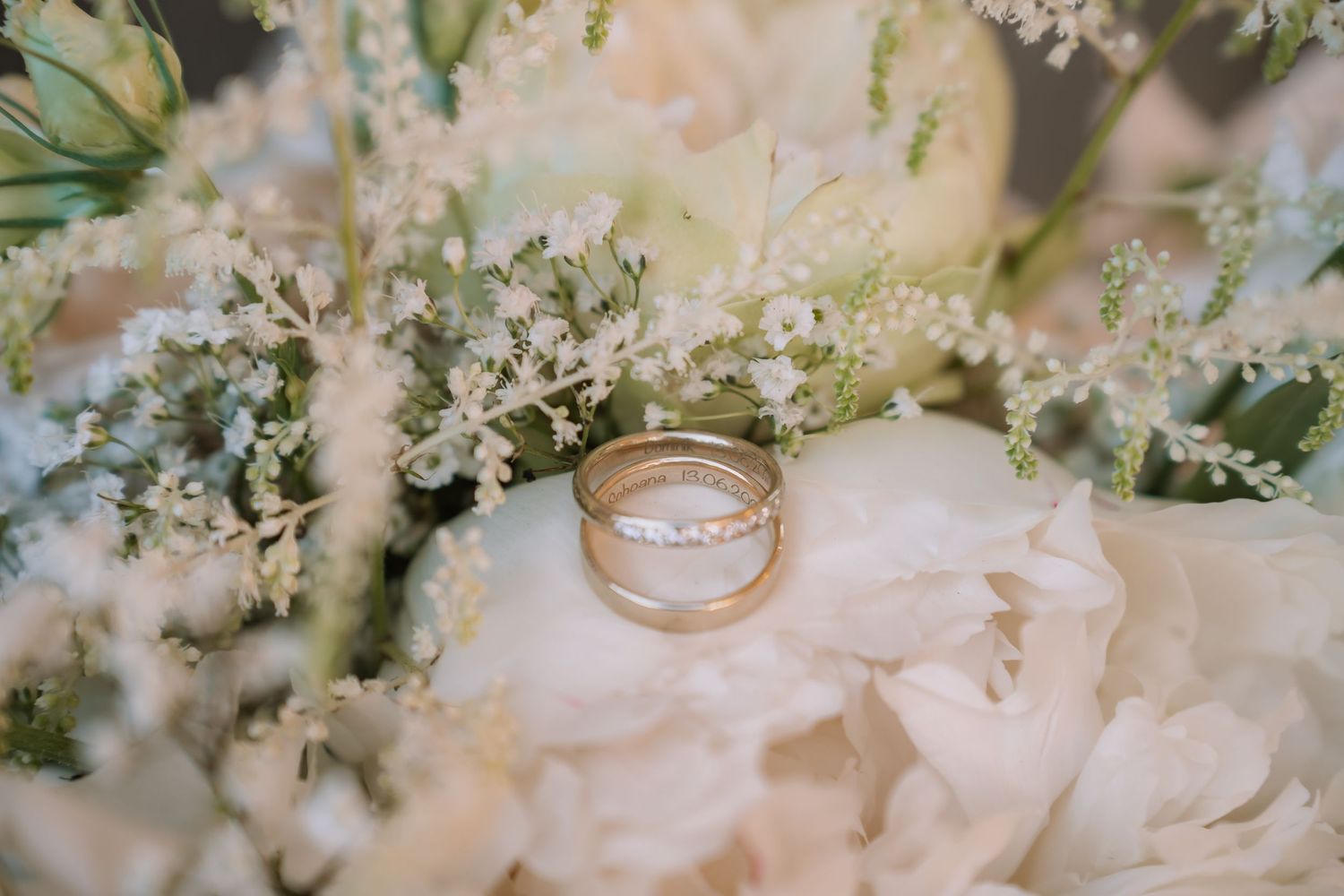 Hochzeitsfotograf Heilbronn,Stuttgart. roots & wandeGold wedding bands resting on a white peony bouquet with delicate baby's breath flowers.