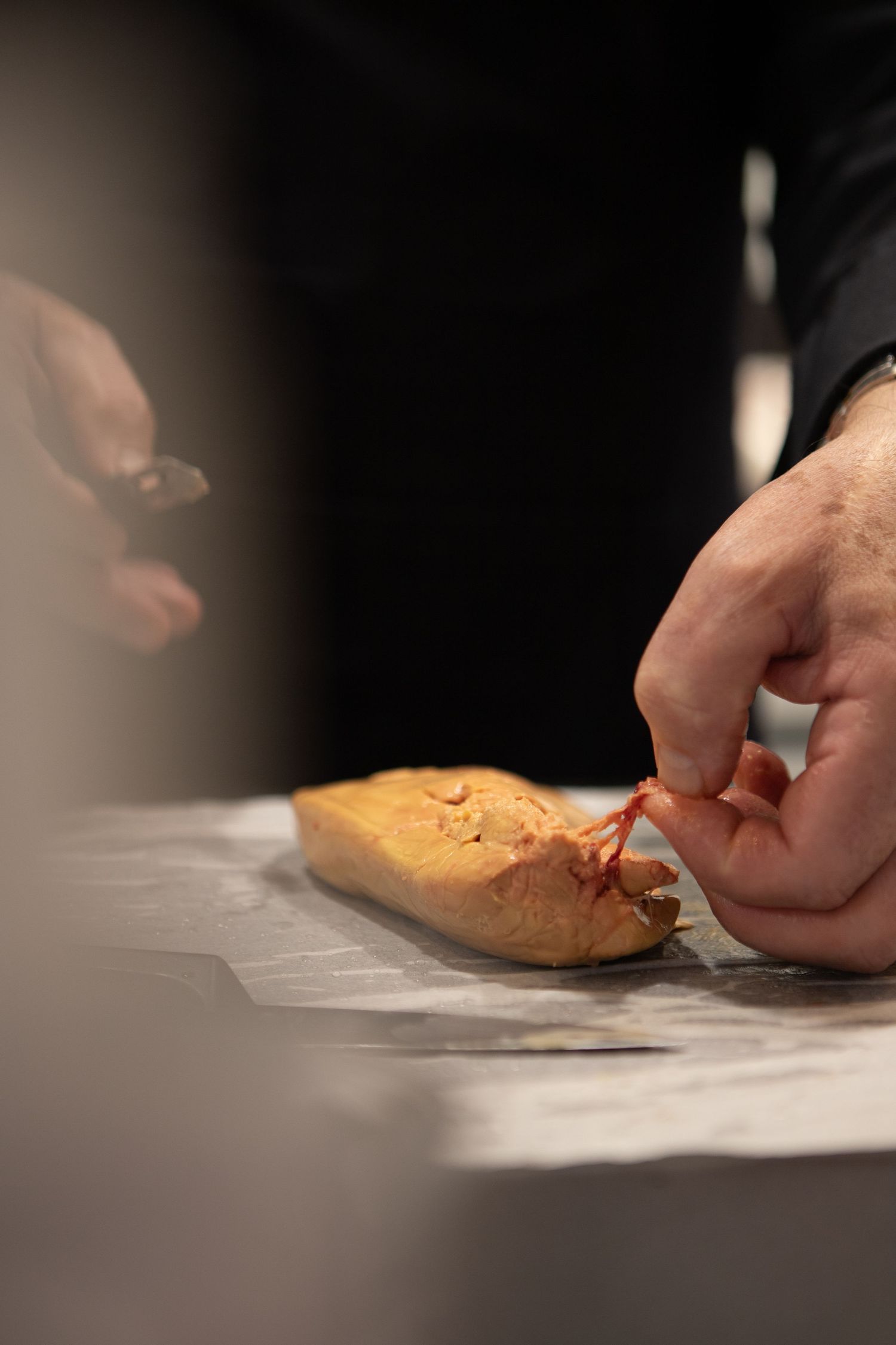 Mains préparant de la nourriture sur une surface sombre sous un éclairage dramatique.