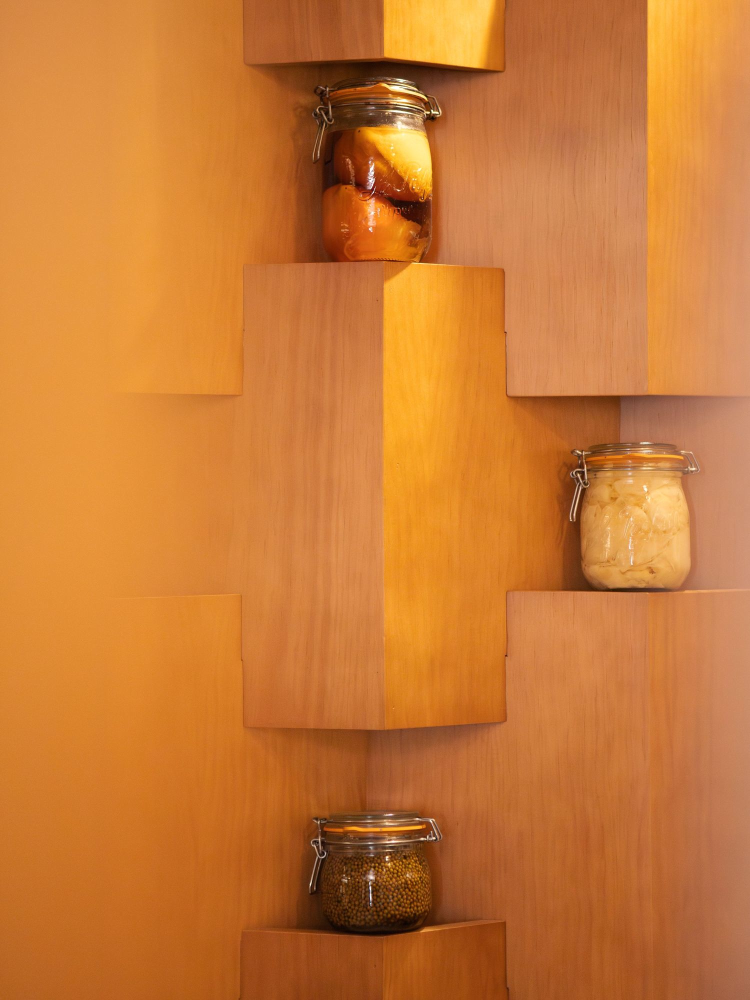 Bocaux en verre contenant des aliments en conserve disposés sur des étagères d'angle en bois avec un éclairage chaleureux.