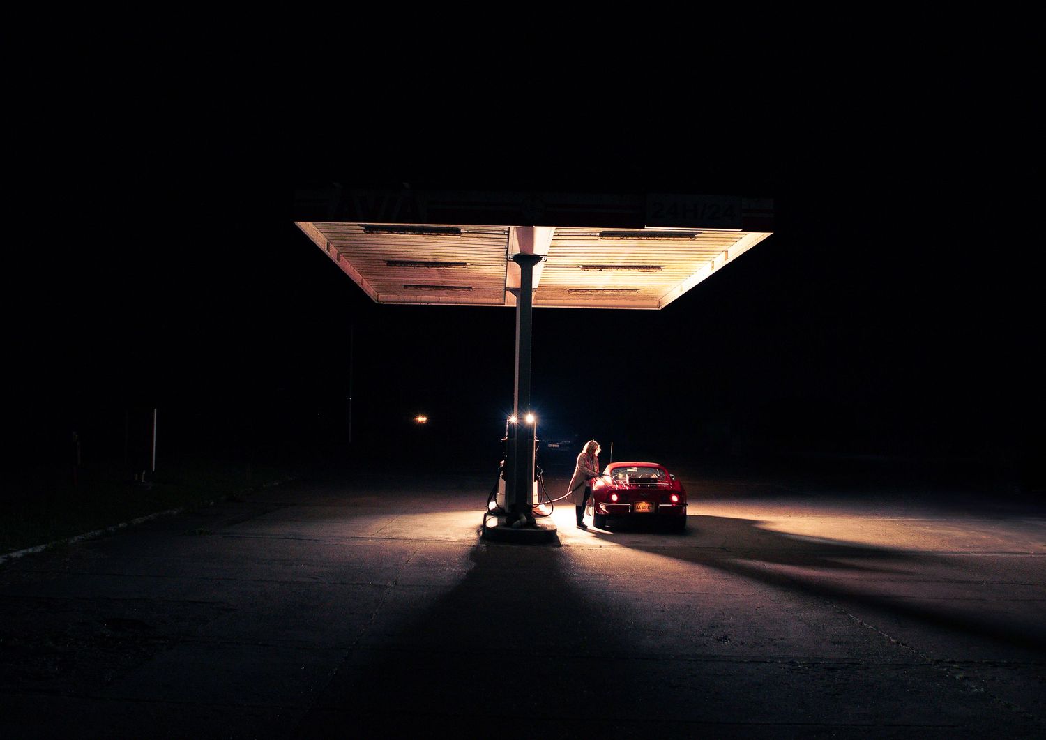 Scène nocturne sombre et atmosphérique avec un éclairage dramatique et des silhouettes de voitures.