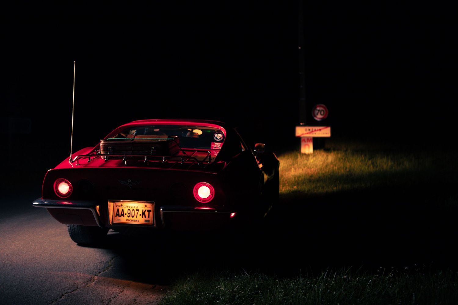 Scène nocturne d'une voiture vintage avec des feux arrière rouges brillants dans une rue sombre.
