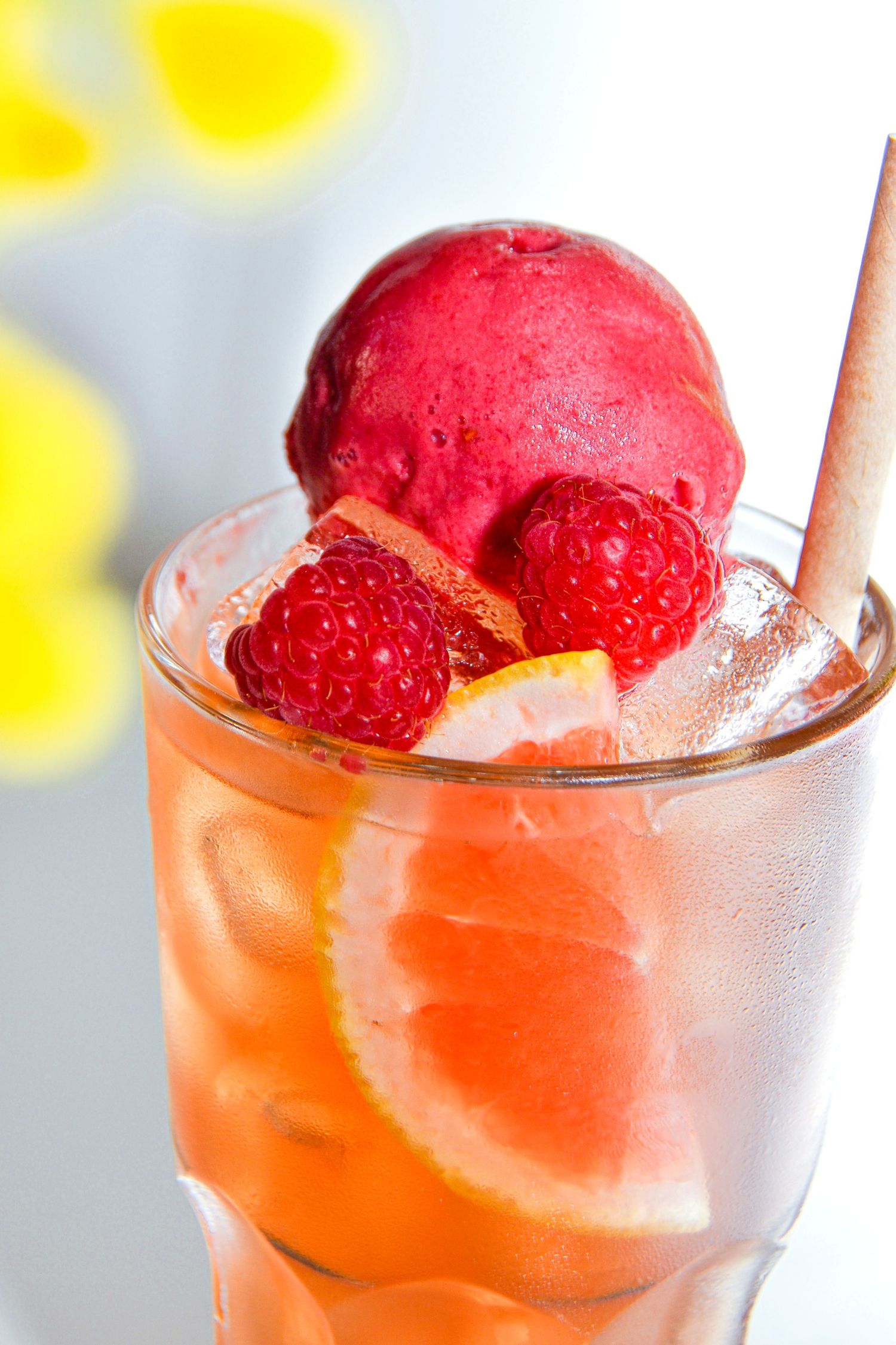 Cocktail rafraîchissant avec sorbet rouge framboise, tranches d'agrumes et garniture de menthe dans un verre givré.