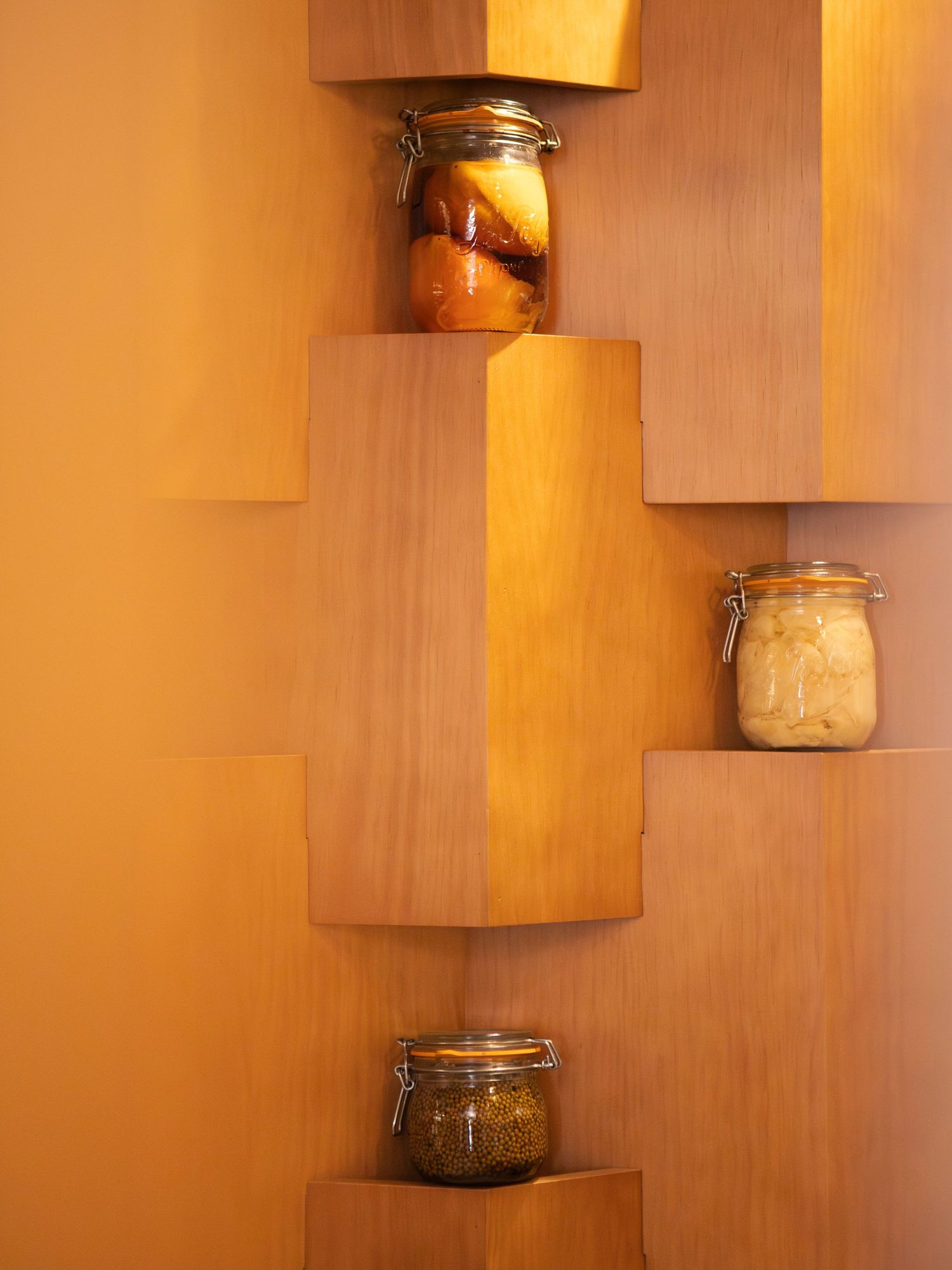 Étagères en bois présentant des bocaux en verre dans un éclairage chaleureux sur un fond en bois d'érable.