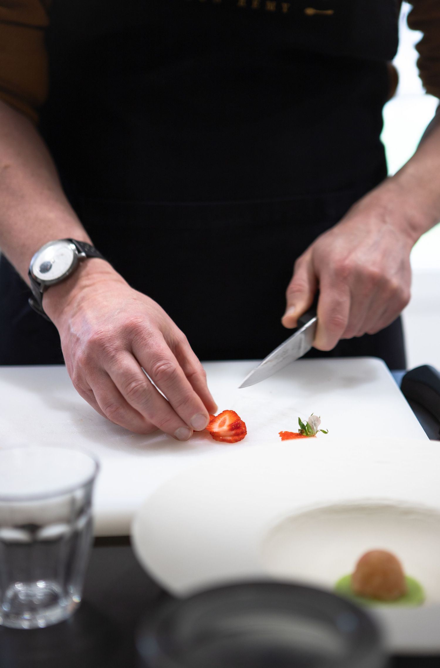Les mains du chef coupent avec précision les ingrédients fruitiers sur une surface blanche.