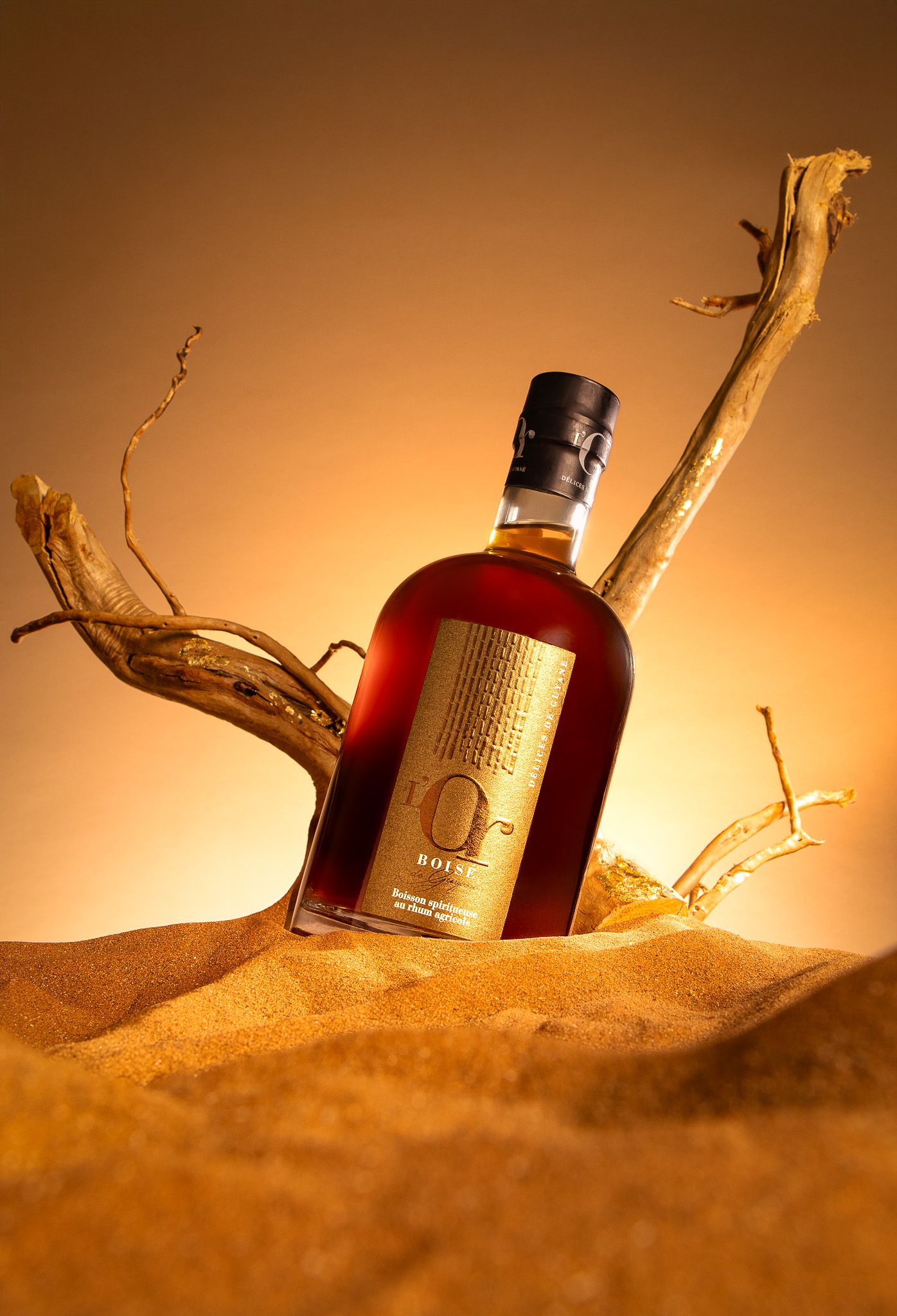 Bouteilles de rhum éclairées de manière artistique et disposées dans le sable du désert avec des accents de bois patiné.