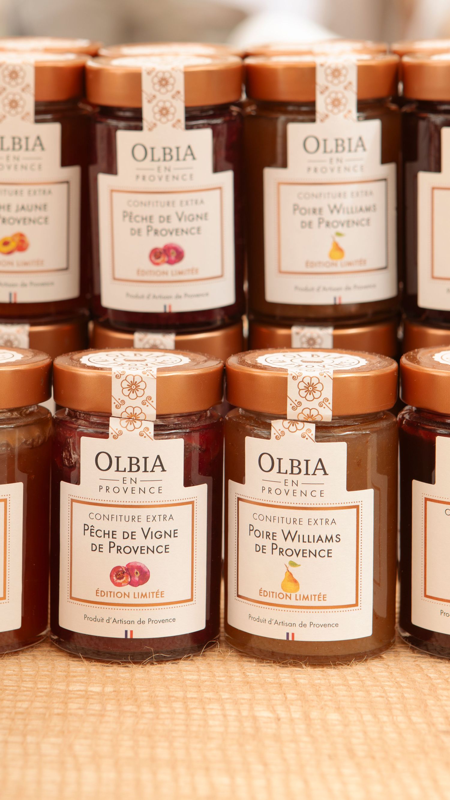 Des rangées de conserves et de confitures gastronomiques de la marque Olbia exposées sur une étagère.
