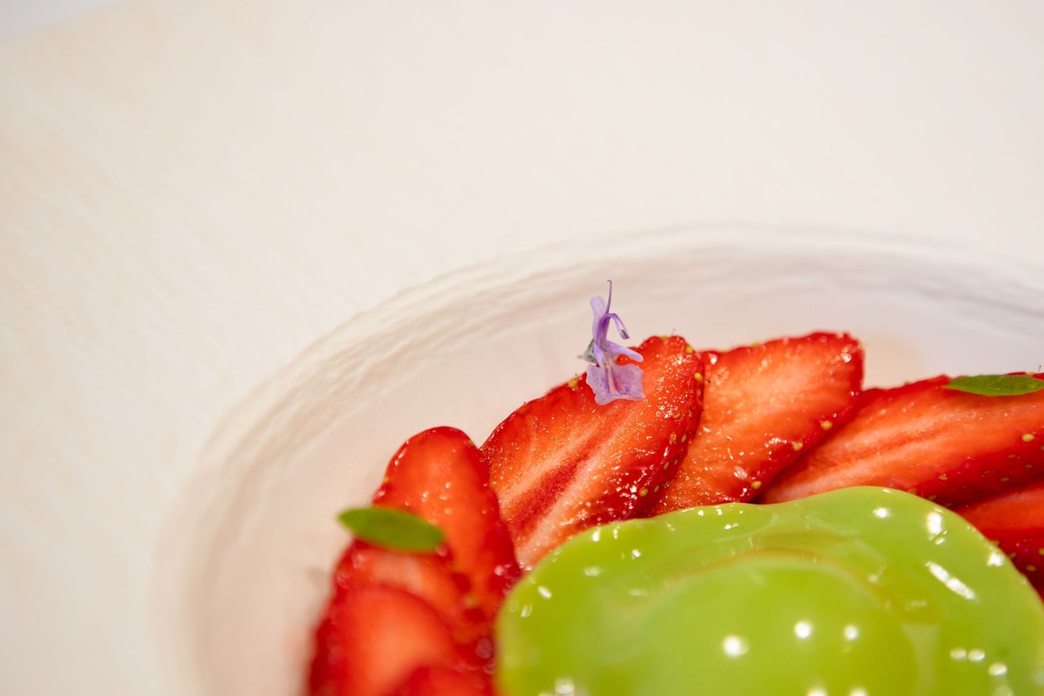 Fraises fraîches et garniture verte disposées sur une assiette blanche.