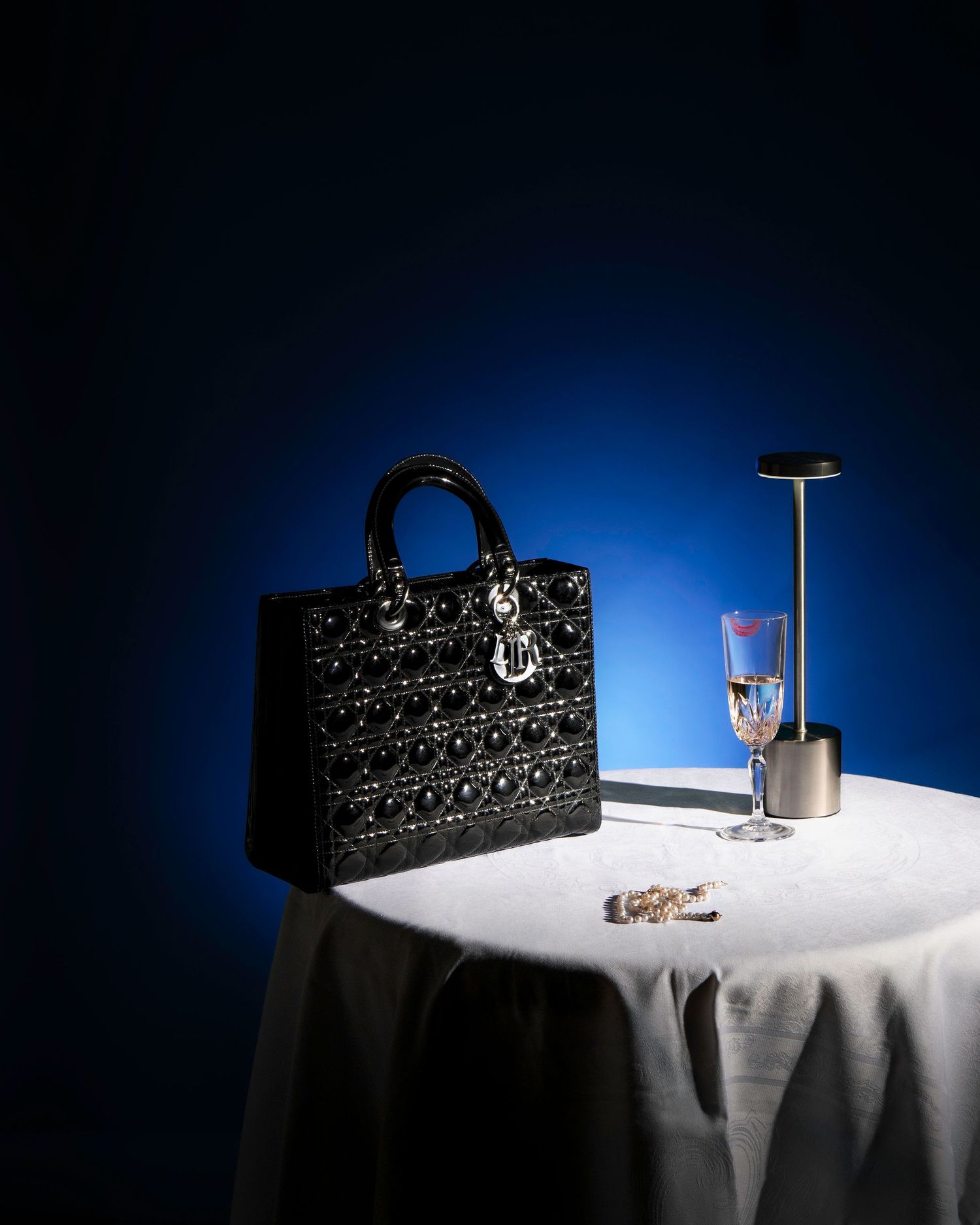 Décoration de table élégante avec sac à main noir et verres à vin sur fond bleu.