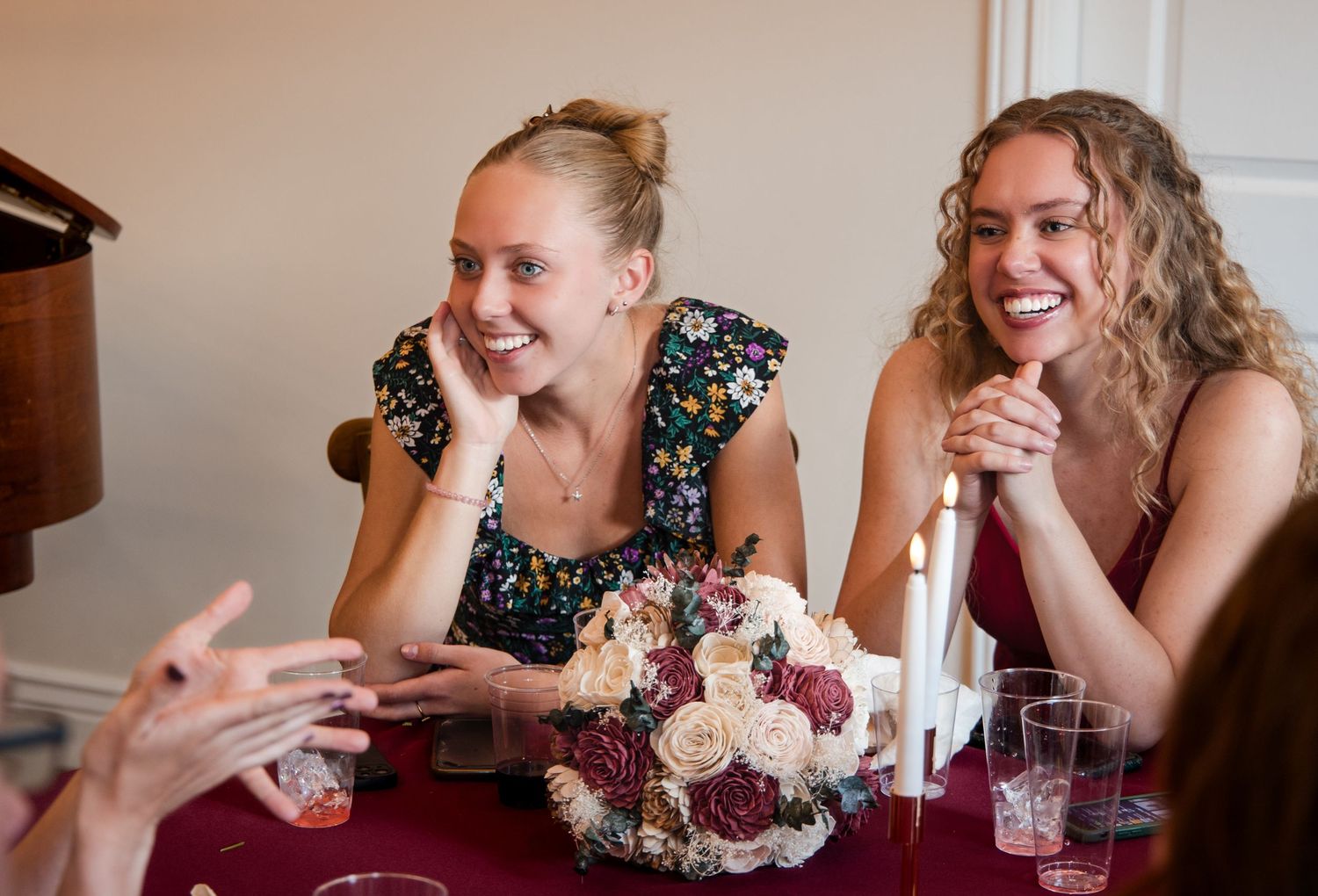 Two people share a laugh while sitting at a table with a burgundy tablecloth and floral bouquet centerpiece.