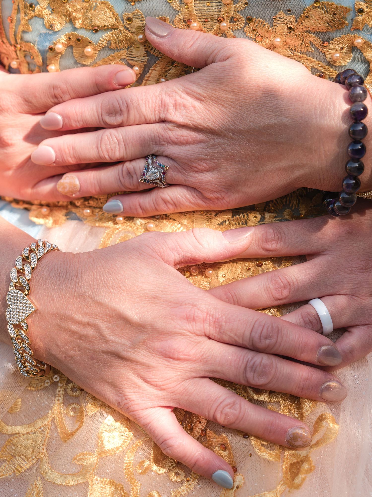 Hands adorned with engagement ring, wedding band, and beaded bracelet displayed against a golden textured background.