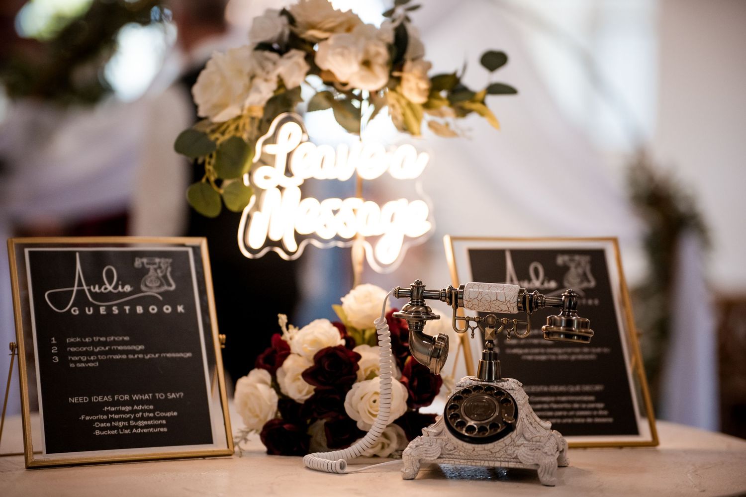 Elegant wedding reception table decor with black framed menus, white flowers, and a decorative neon sign glowing.