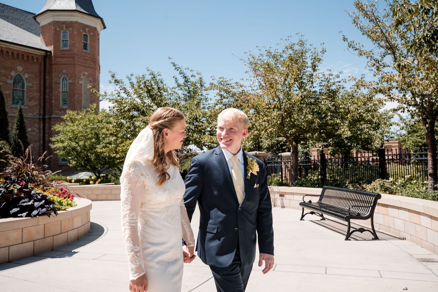 A bride and groom walk together on a sunny day outside the Provo City Center LDS temple.