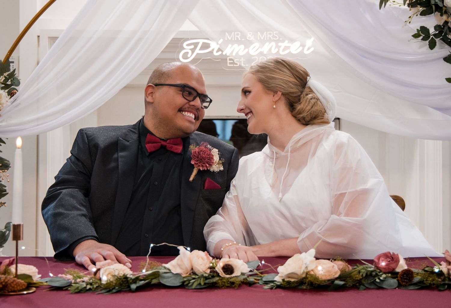 A happy couple shares a joyful moment together at their wedding reception with white draping and floral decorations.