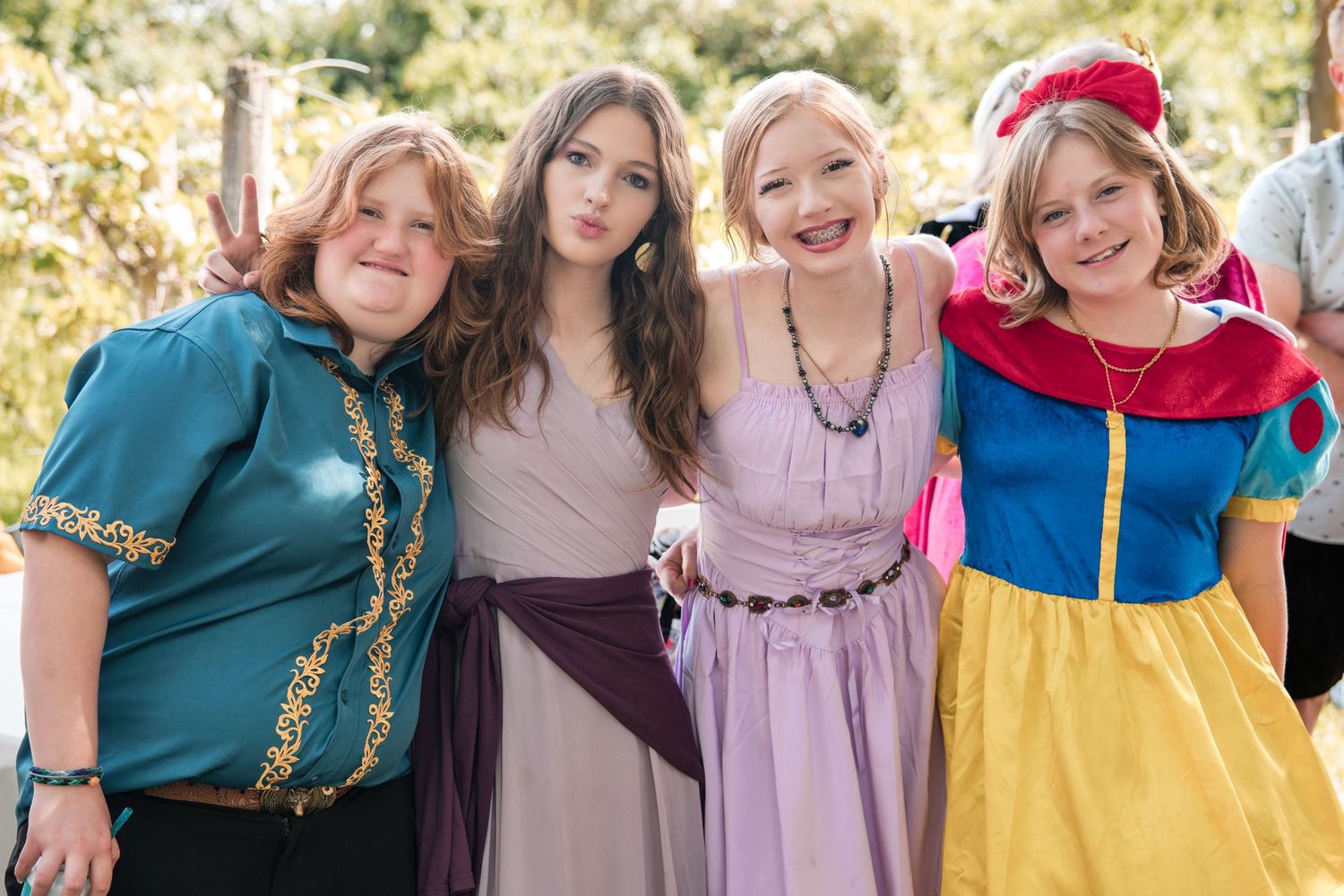 A smiling group wearing colorful princess-inspired dresses poses together in an outdoor setting during a party.