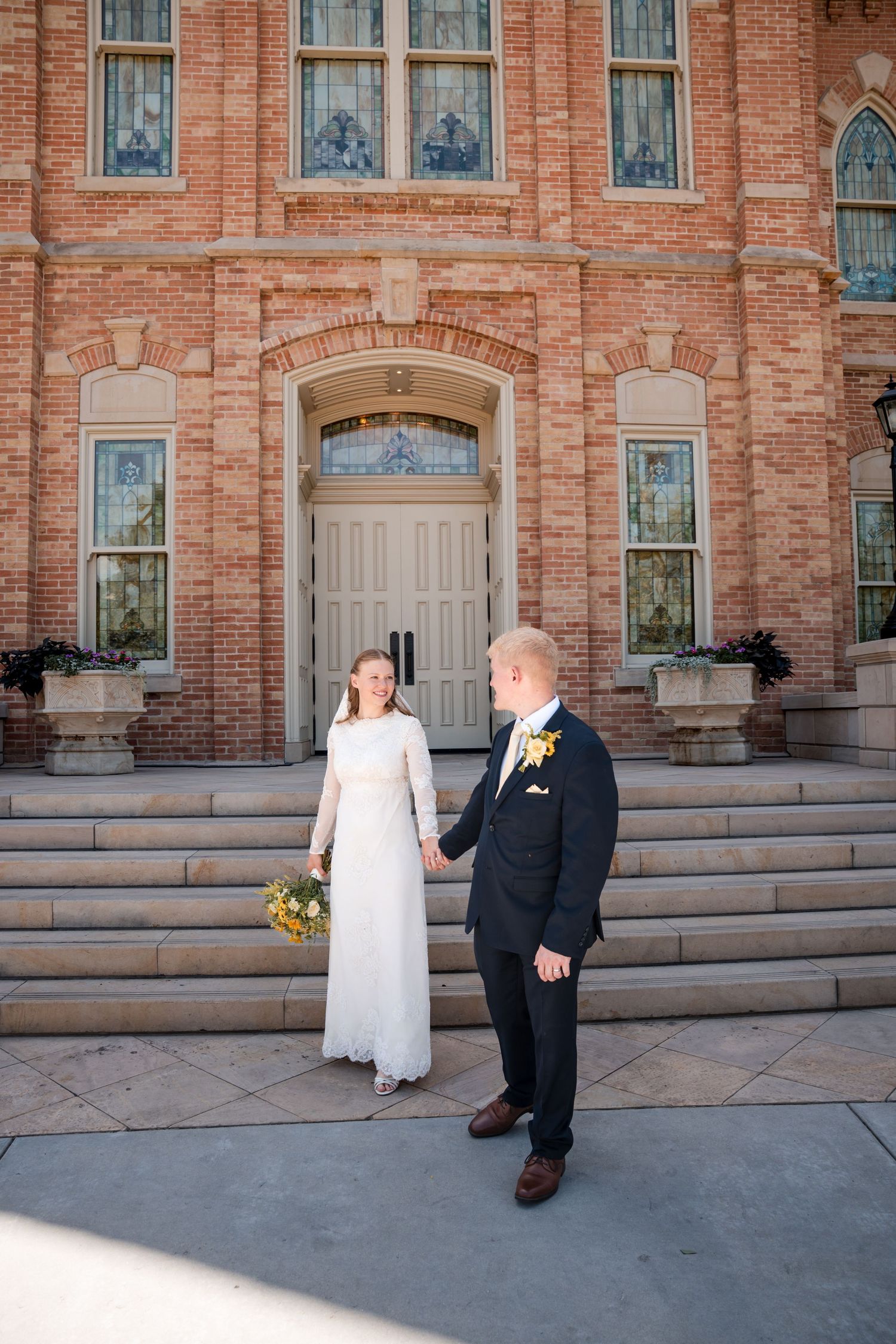 A couple stands on the steps of the Provo City Center LDS temple with Gothic windows on their wedding day.