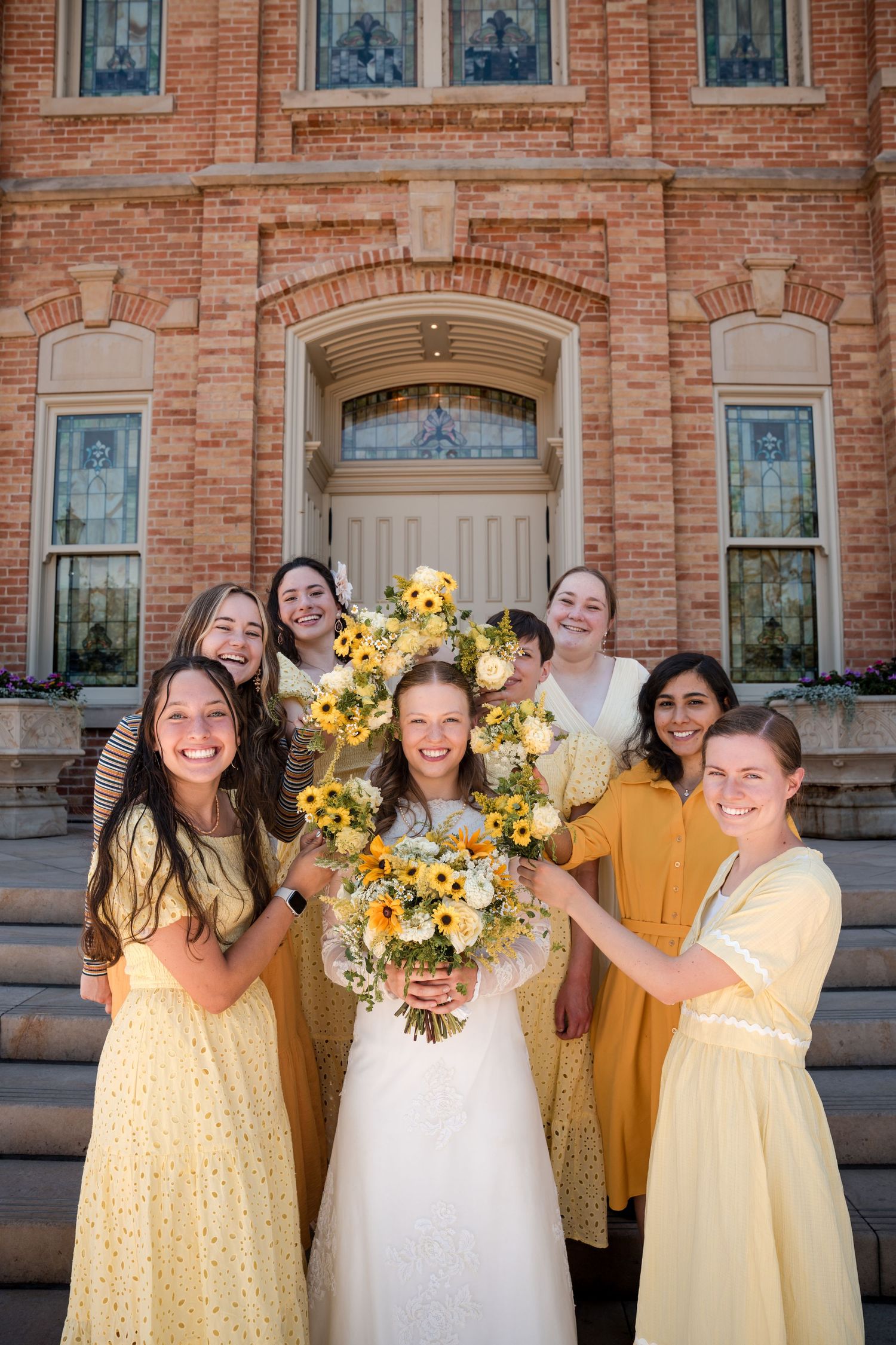 Bridal party in sunny yellow polka dot dresses and white wedding gown pose together outside the Provo City Center LDS Temple.