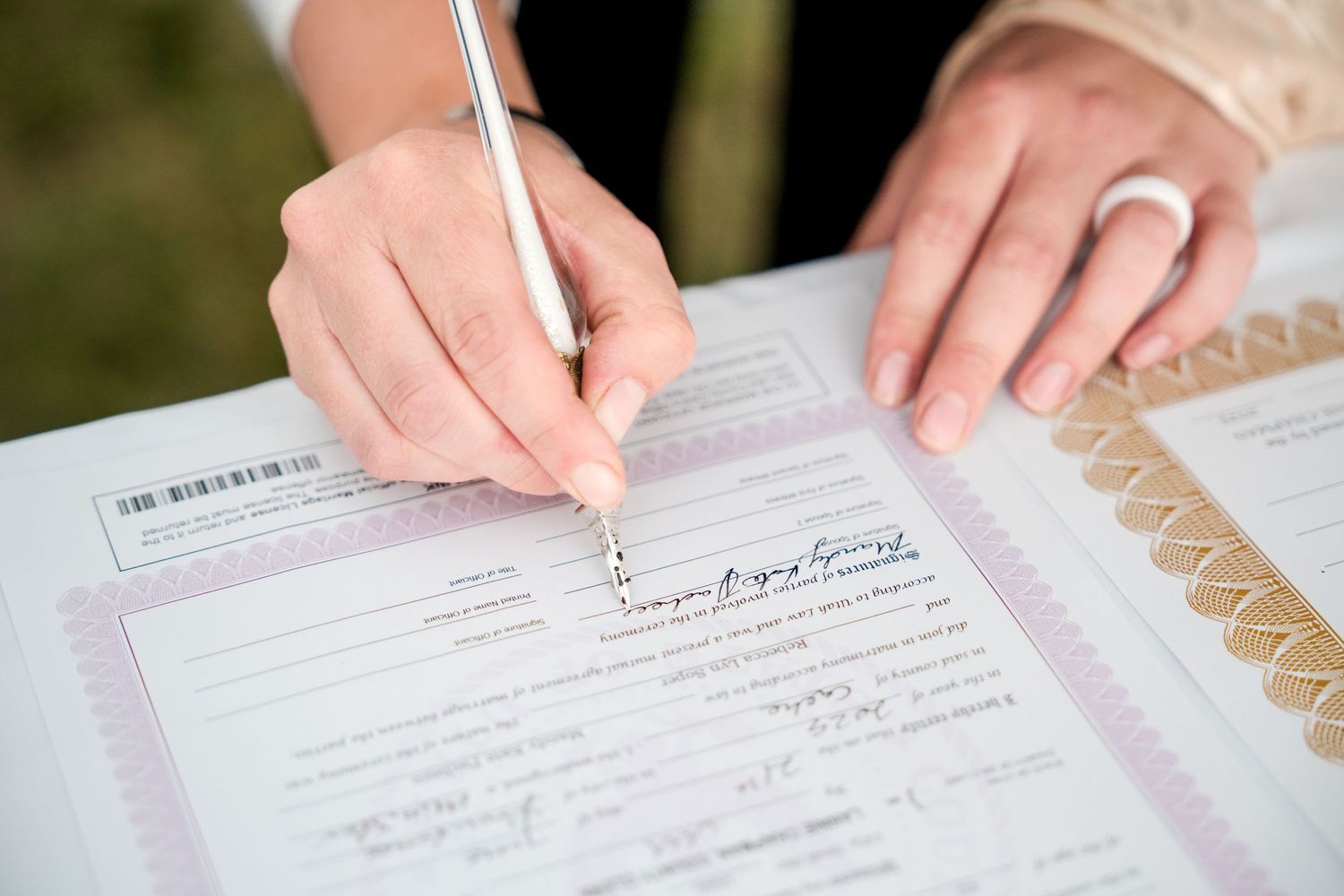 A bride and groom's hands signing official marriage documents at a registry ceremony.