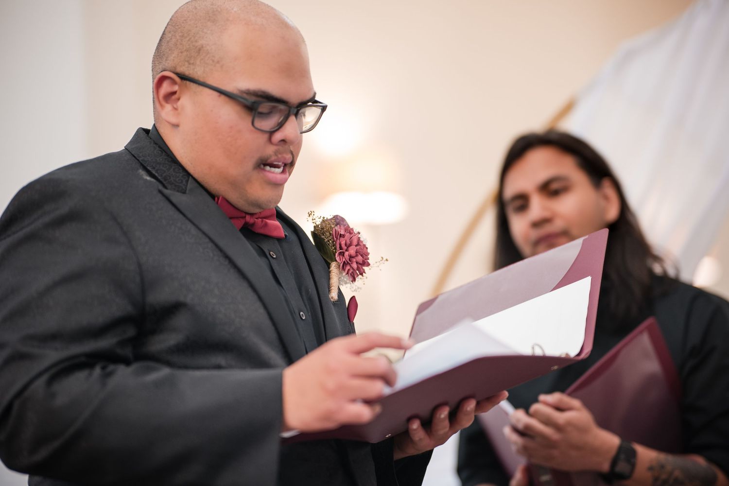 People dressed in formalwear share a laugh while reading from books during an elegant ceremony or event.