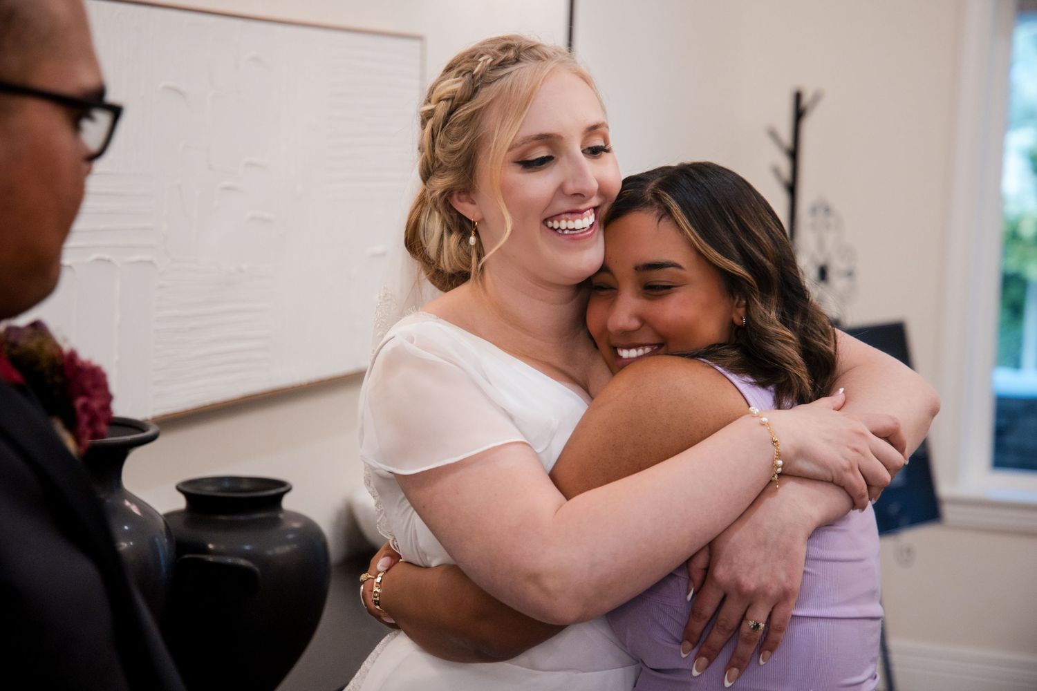 Emotional wedding moment captured as embracing people share tears and laughter in a warm indoor setting.