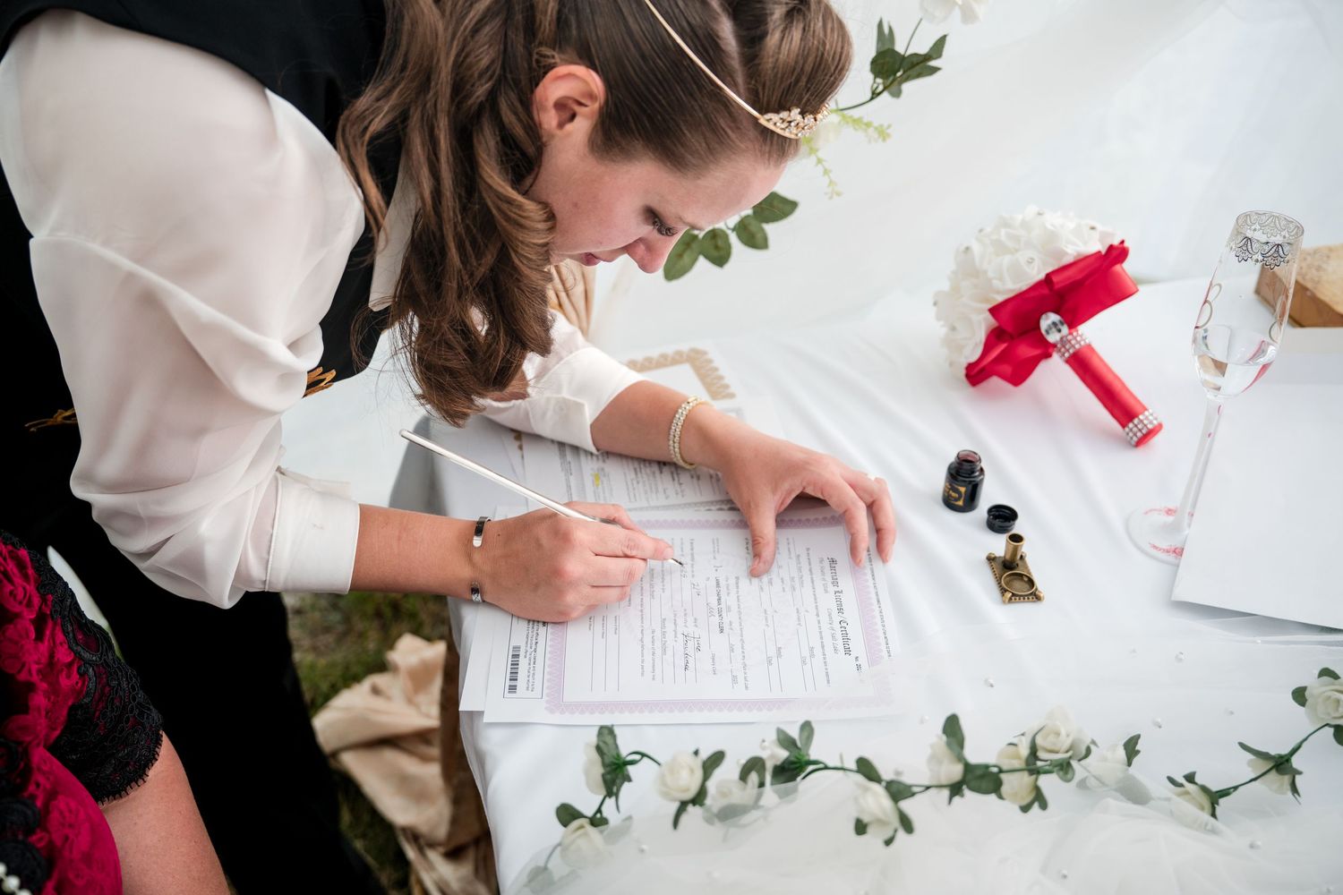 Bride signing the wedding certificate at table decorated with greenery and event planning supplies.
