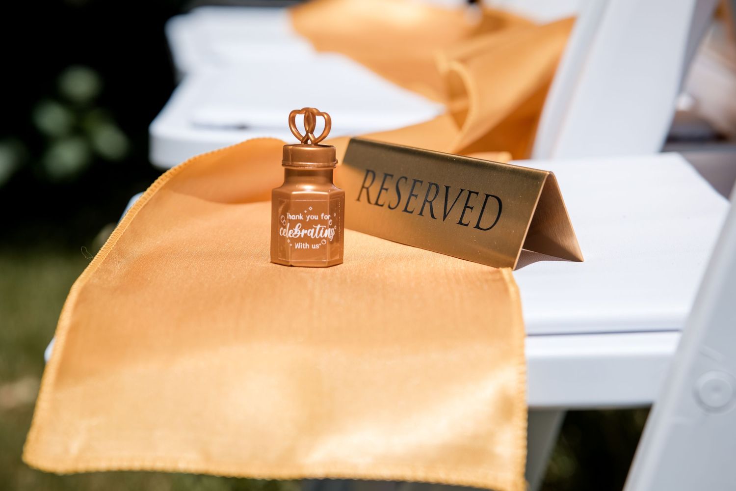 A small perfume bottle and reserved sign displayed on peach-colored fabric at a wedding reception setup.