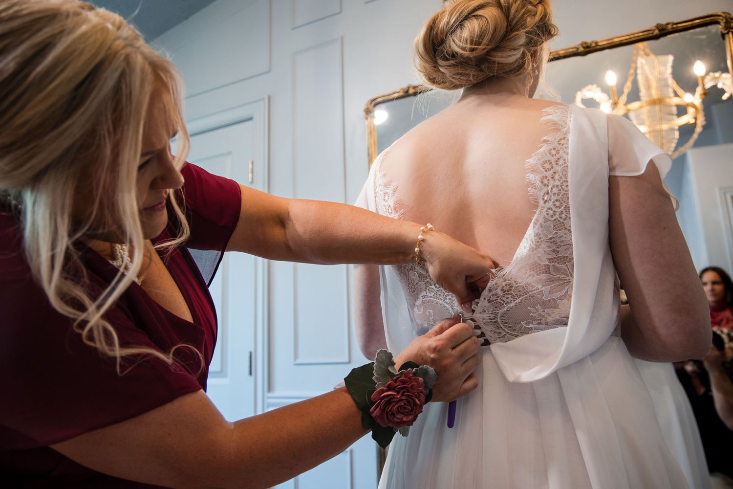 People helping adjust a flowing white wedding dress before a ceremony.
