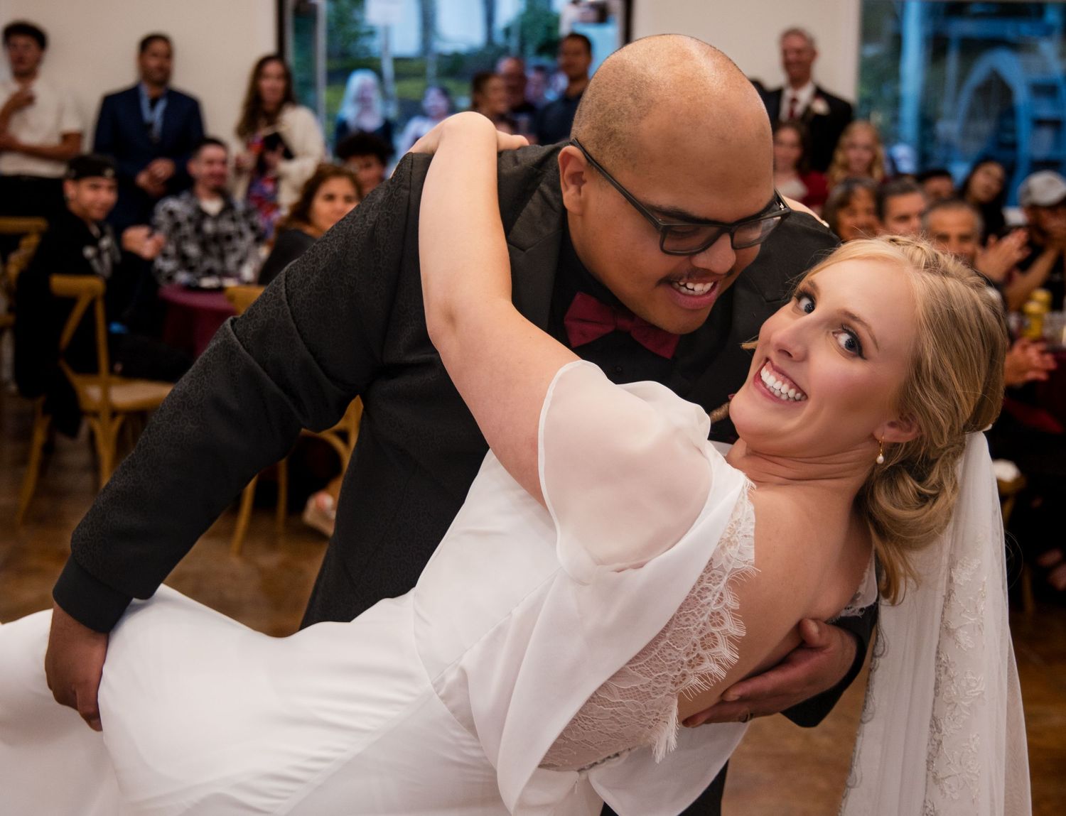 A joyful couple shares a romantic dance dip during their wedding reception with guests looking on in the background.