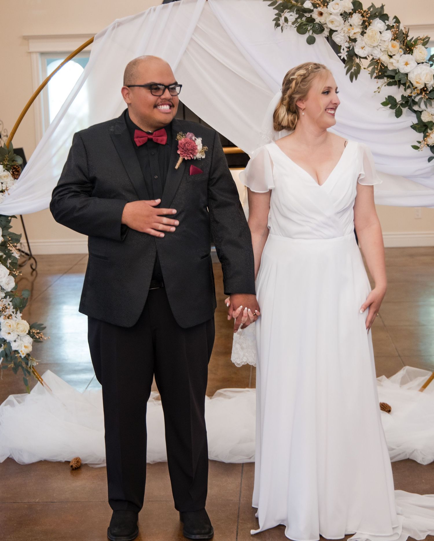 A couple shares a joyful dance moment in a wedding venue decorated with white draping and floral arrangements.