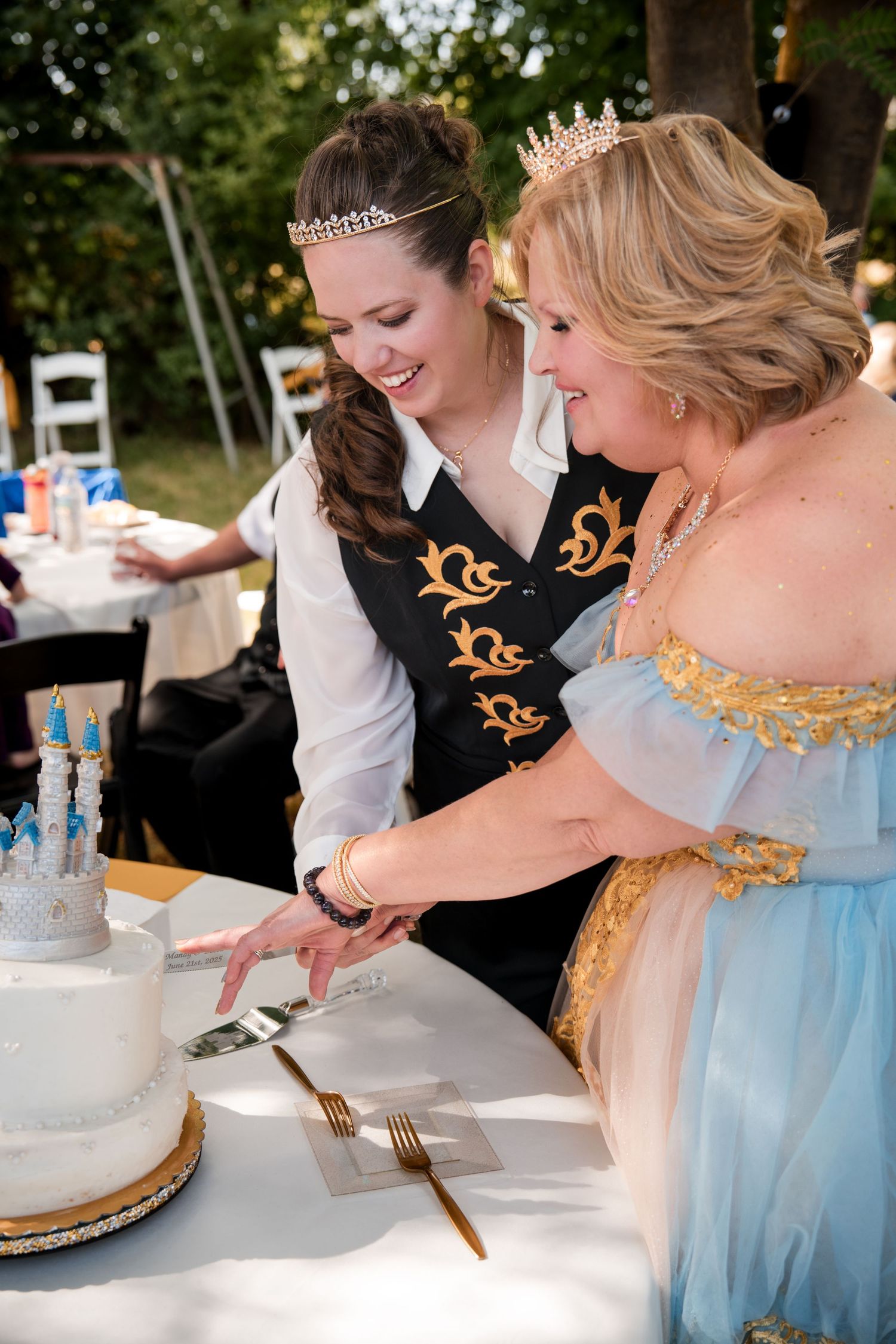 Two Brides in formal attire cutting a white wedding cake at a reception celebration.
