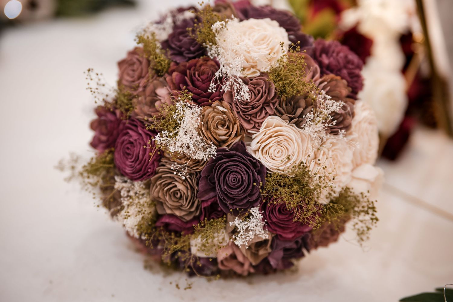 Close up of a vintage-style wedding bouquet featuring dried roses in burgundy, brown and beige with baby's breath accents.