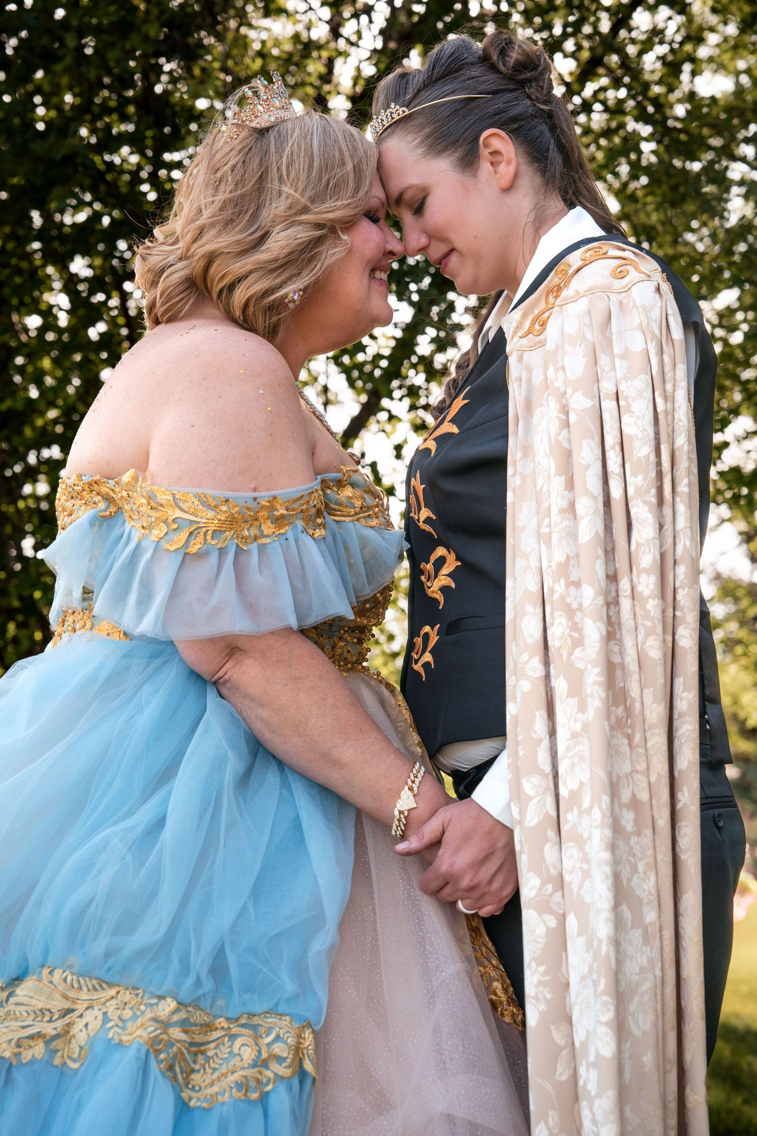 Two people in romantic fantasy costumes share an intimate moment in a garden setting while holding hands.