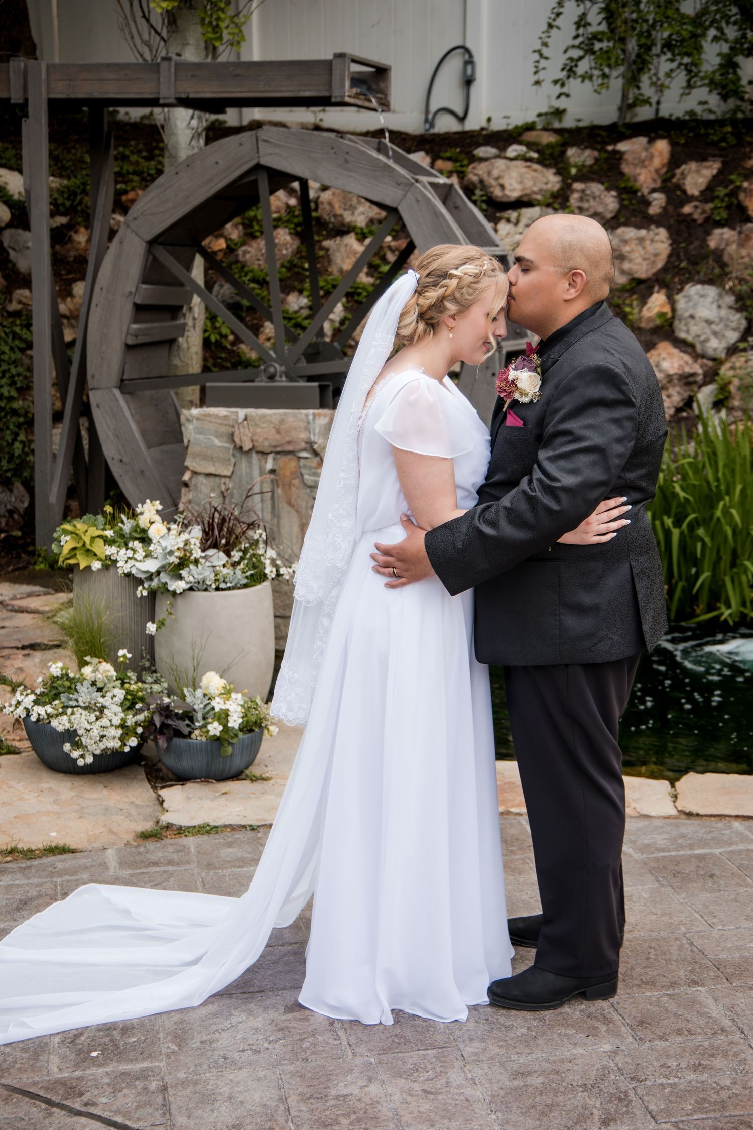 A couple shares a romantic kiss in matching white and black formal attire during a wedding ceremony.