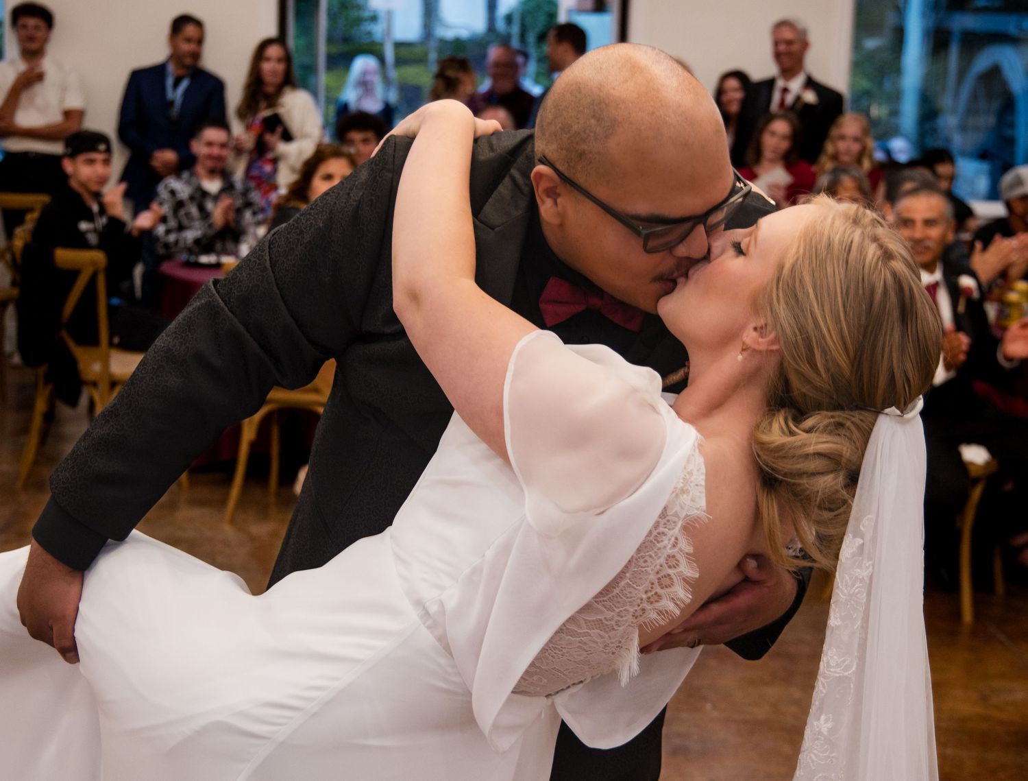 A couple shares a romantic dip kiss during their first dance on the wooden floor of their wedding reception.