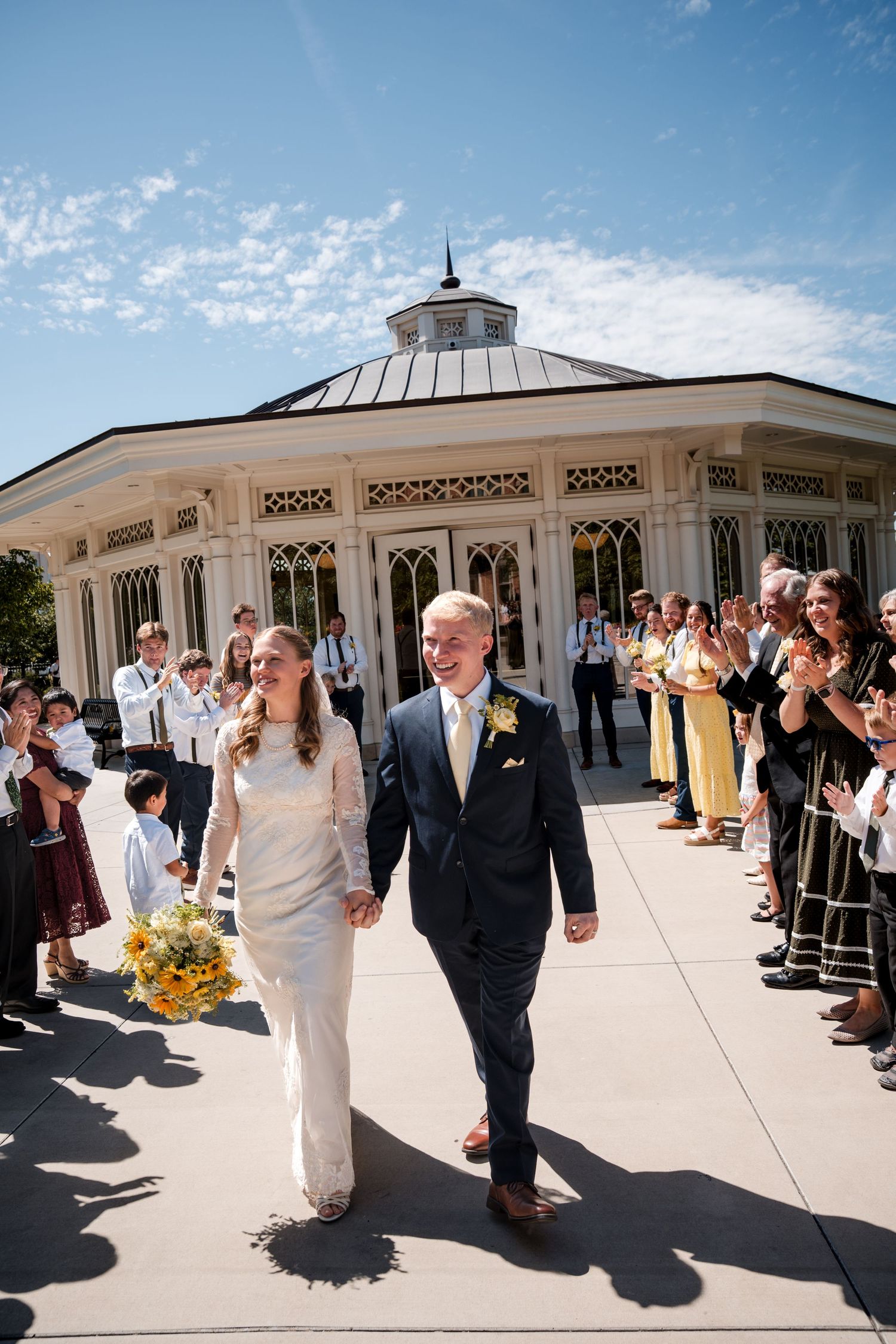 A progression of five wedding photos showing a couple walking together amidst outdoor guests on a sunny day.