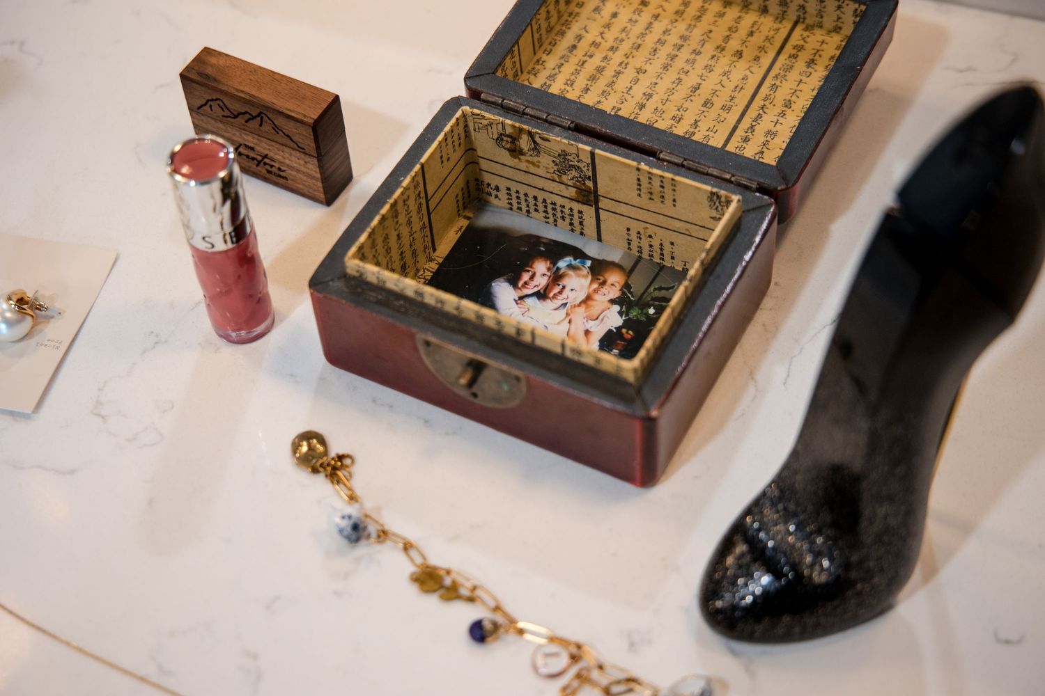 A display of wooden boxes with jewelry and vintage accessories arranged alongside a black shoe on a white surface.